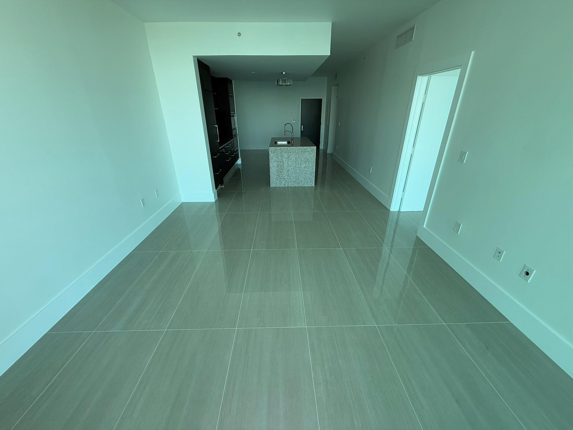 Open-concept living space featuring sleek tile flooring throughout, a central island with a stone-finish countertop, and dark wood-finish cabinetry