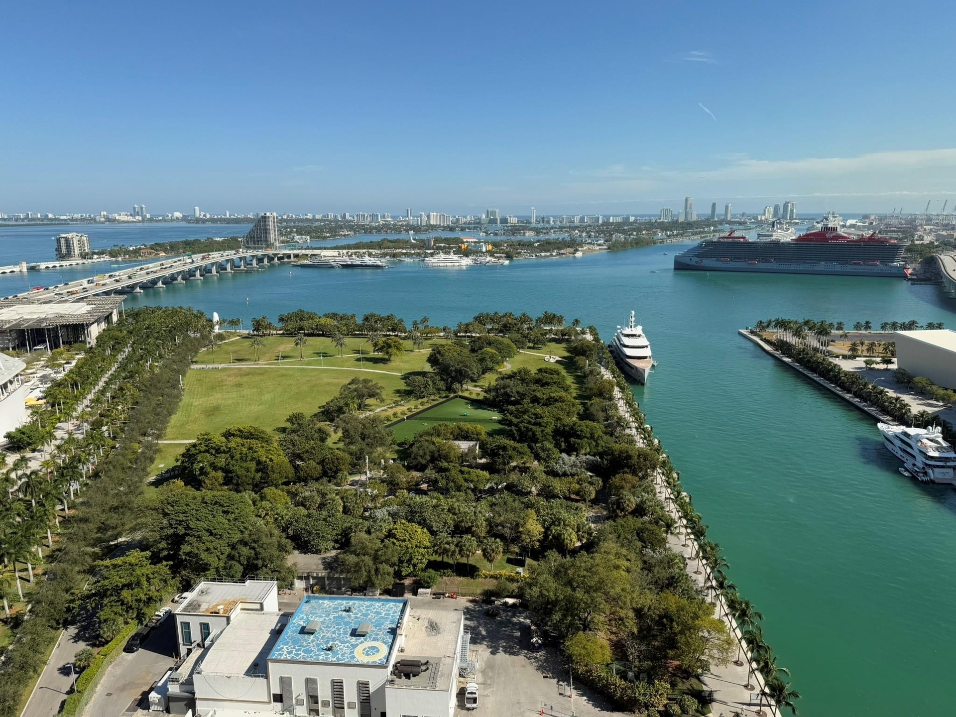 Expansive waterfront panorama showcasing a prominent waterway, an urban skyline, a multi-lane bridge, extensive green spaces, and multiple marine vess