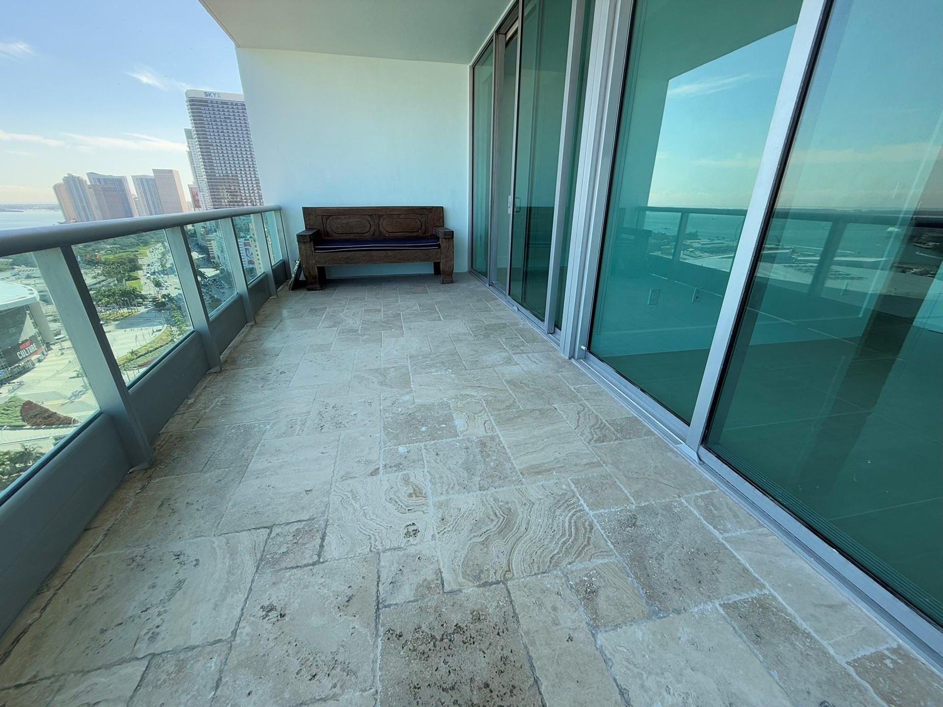 Spacious balcony featuring stone tile flooring, clear glass railing, and floor-to-ceiling sliding glass doors