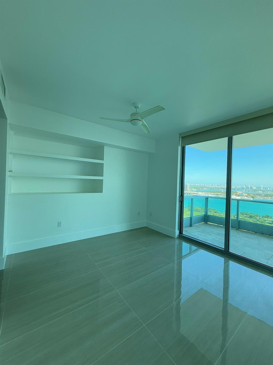 Spacious room featuring large format tile flooring, built-in shelving, and a ceiling fan