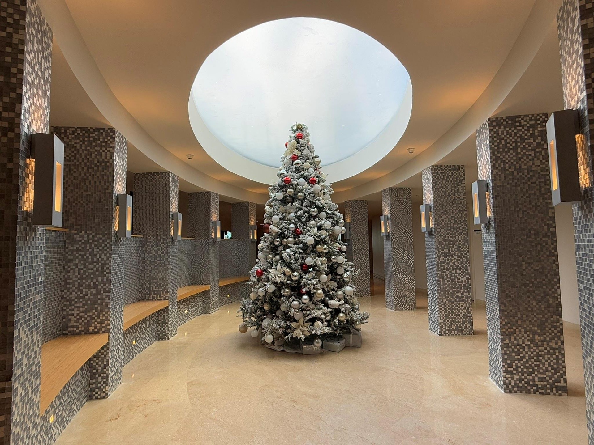 Circular architectural feature with an overhead skylight, surrounded by mosaic-tiled columns