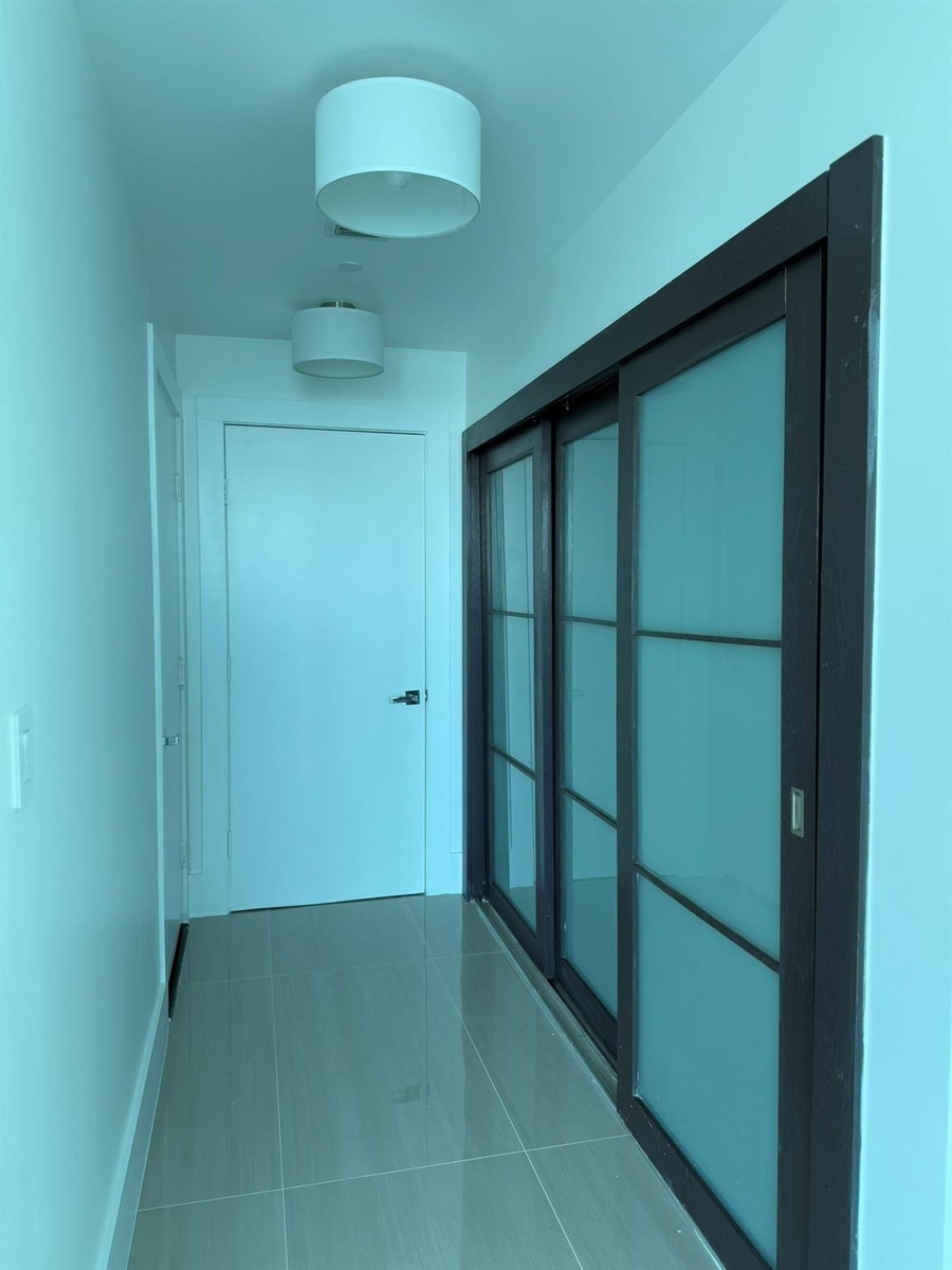 Hallway featuring large format tile flooring, modern flush-mount lighting, and dark-framed sliding doors with frosted glass panels