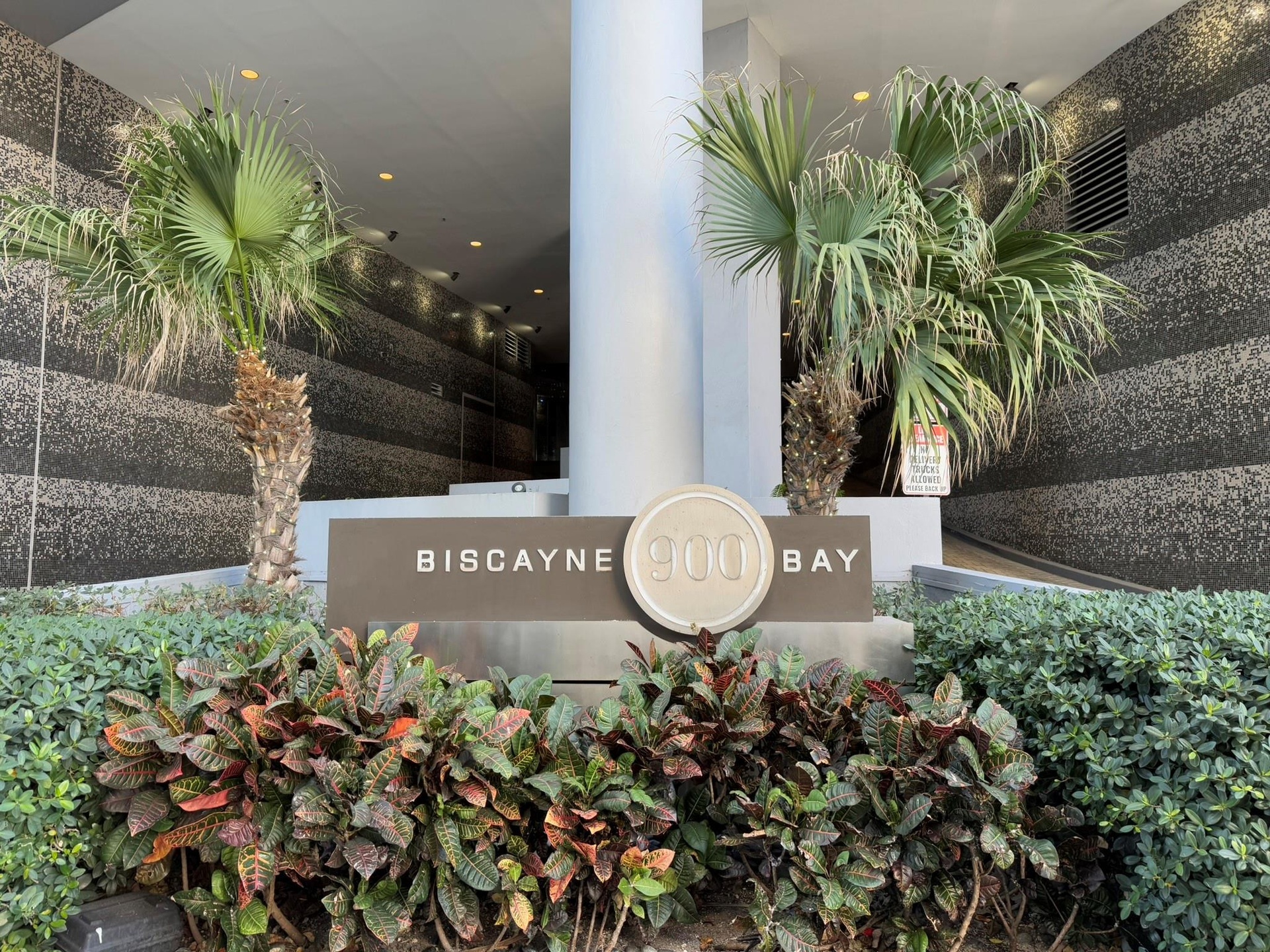Contemporary building entrance featuring a prominent address sign and lush tropical landscaping