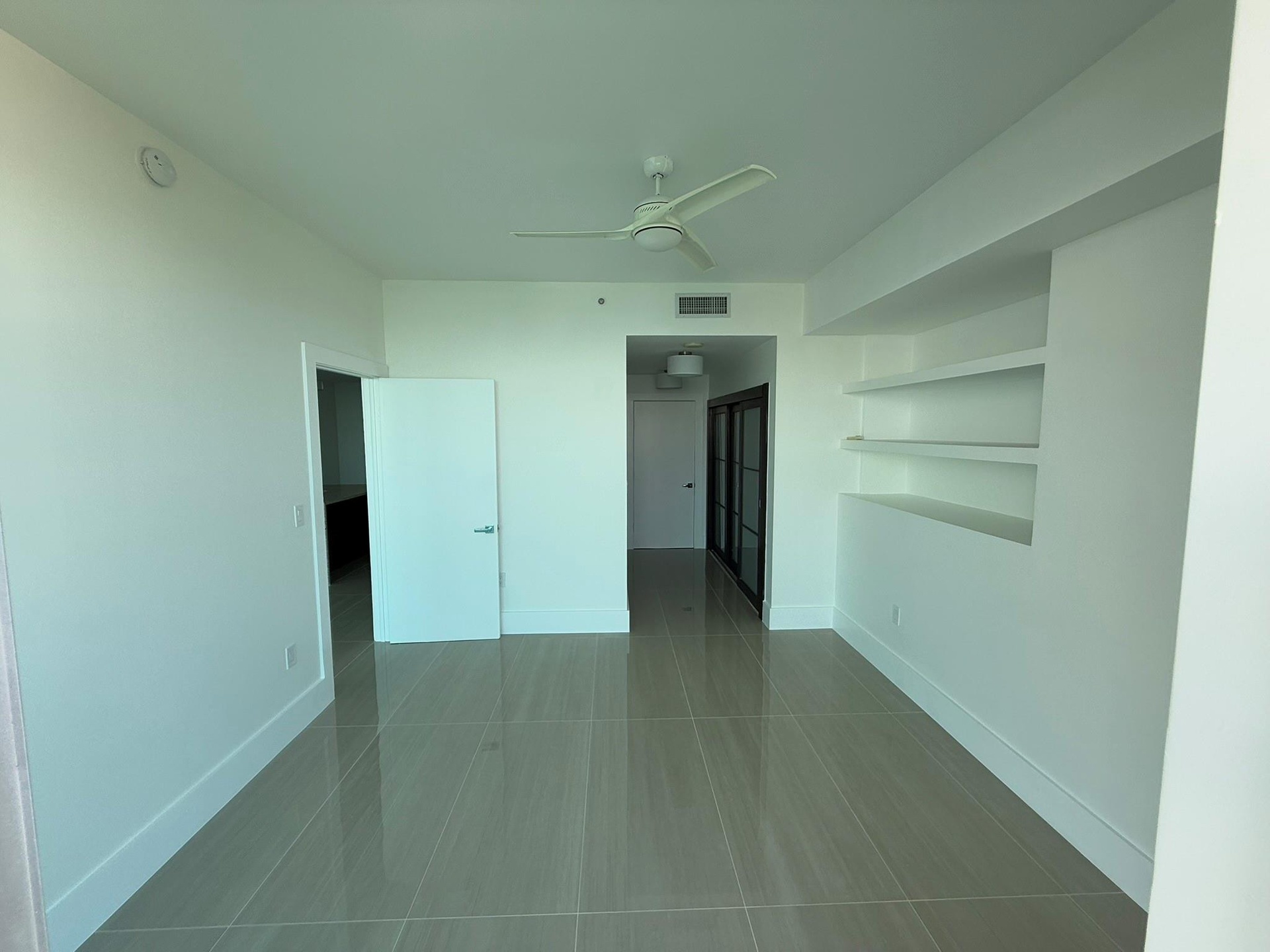 Spacious room featuring large format tile flooring, a contemporary ceiling fan, and built-in shelving