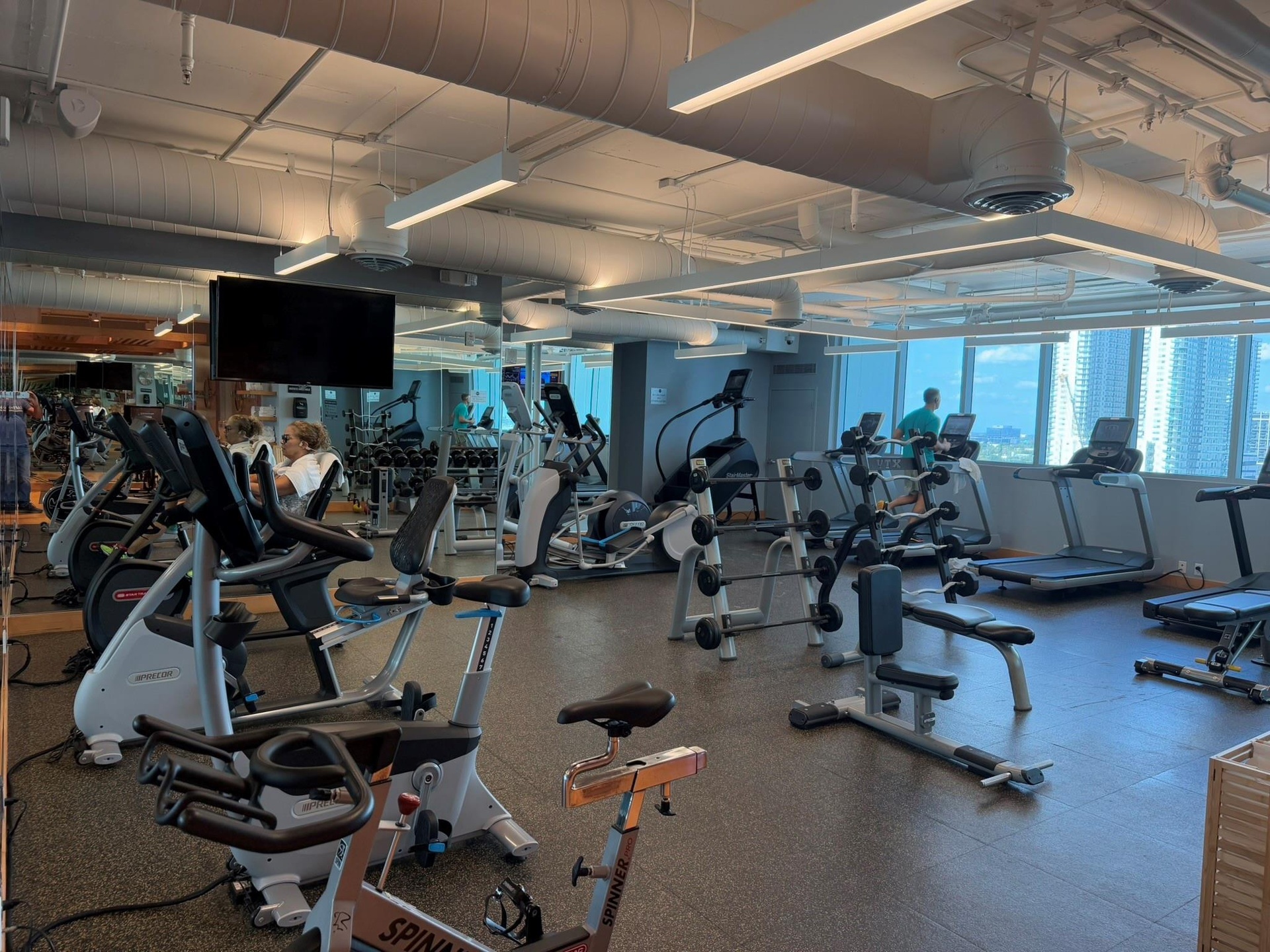 Fitness center featuring high ceilings, exposed ductwork, large windows, multiple exercise machines, and weight training equipment