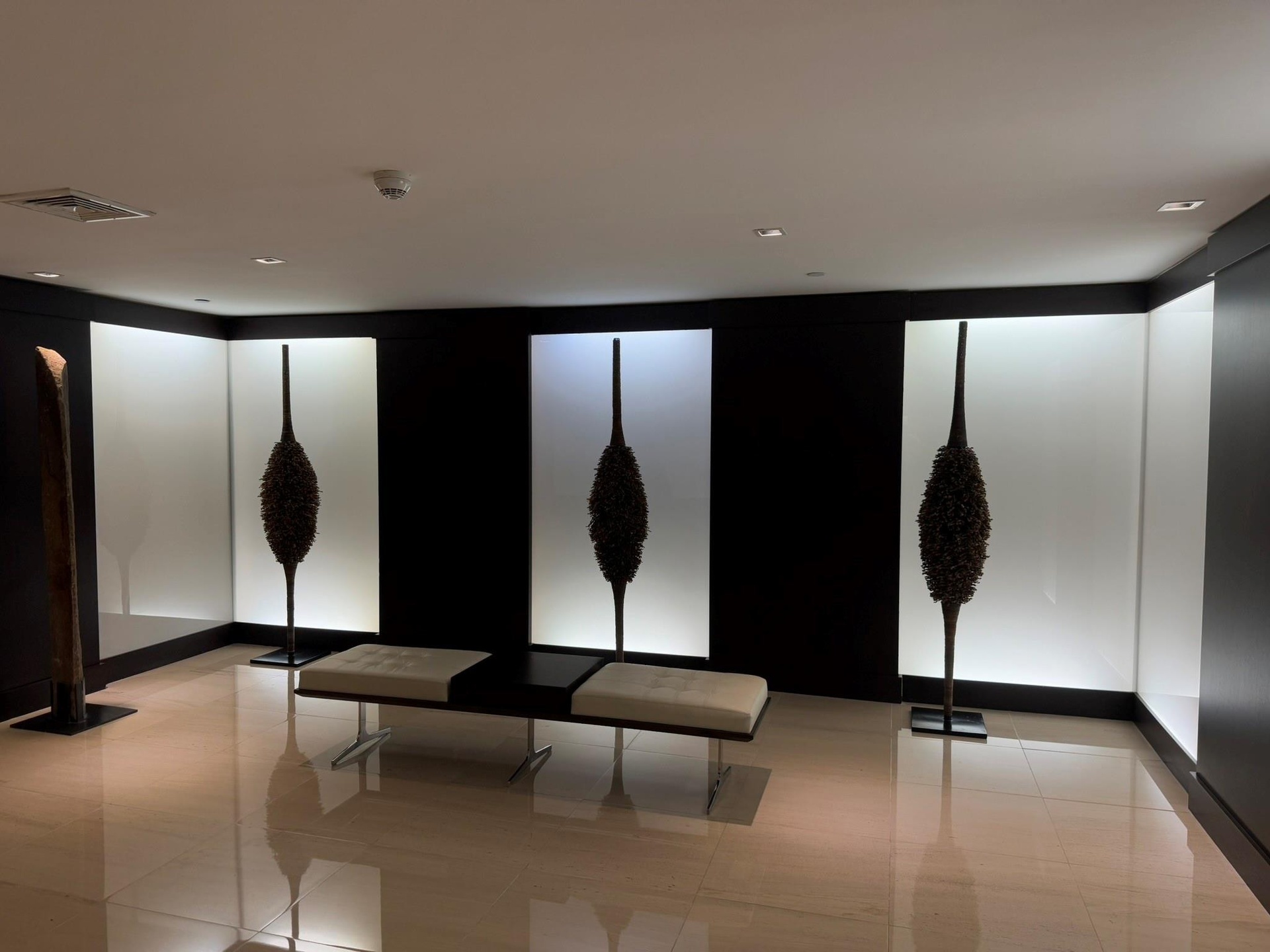 High-gloss tile flooring with recessed ceiling lighting, illuminating a corridor with dark wall panels and backlit display niches
