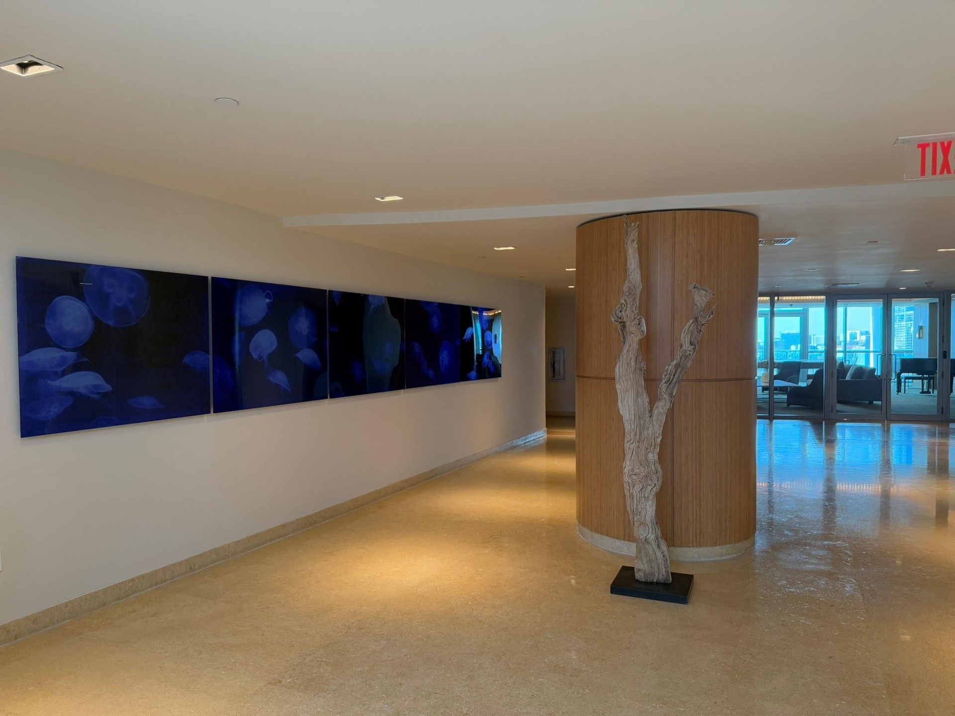 Polished stone flooring extending through a wide corridor, featuring recessed lighting and a wood-paneled column with a decorative sculpture