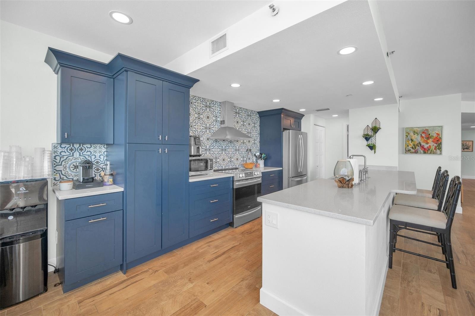Cucina Features Versay Grand Blue Encaustic Style Porcelain Tile Backsplash, Stainless appliances, Quartz Counter Surfaces, Custom Shaker Style Cabine