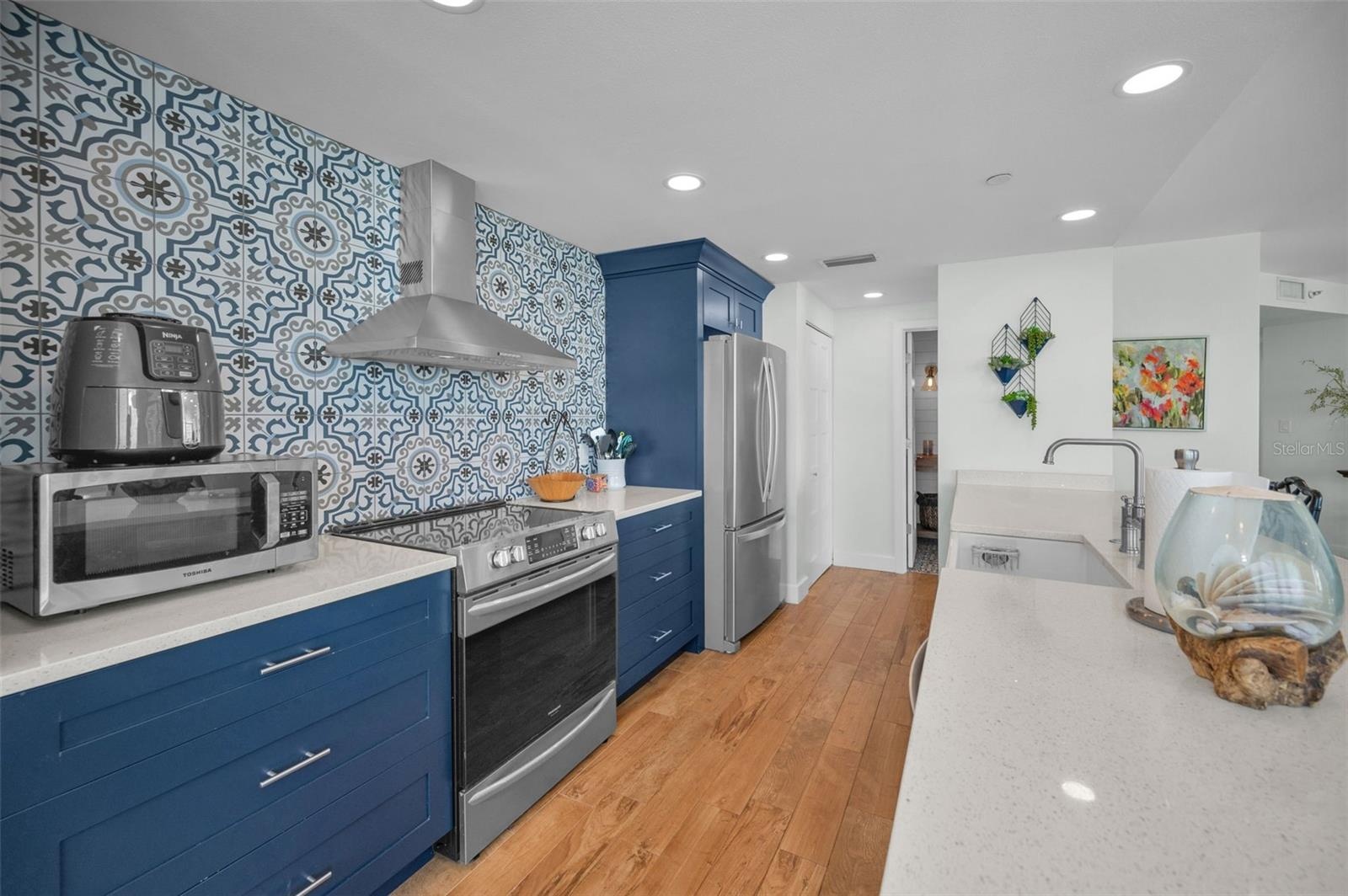 Cucina Features Versay Grand Blue Encaustic Style Porcelain Tile Backsplash, Stainless appliances, Quartz Counter Surfaces, Custom Shaker Style Cabine