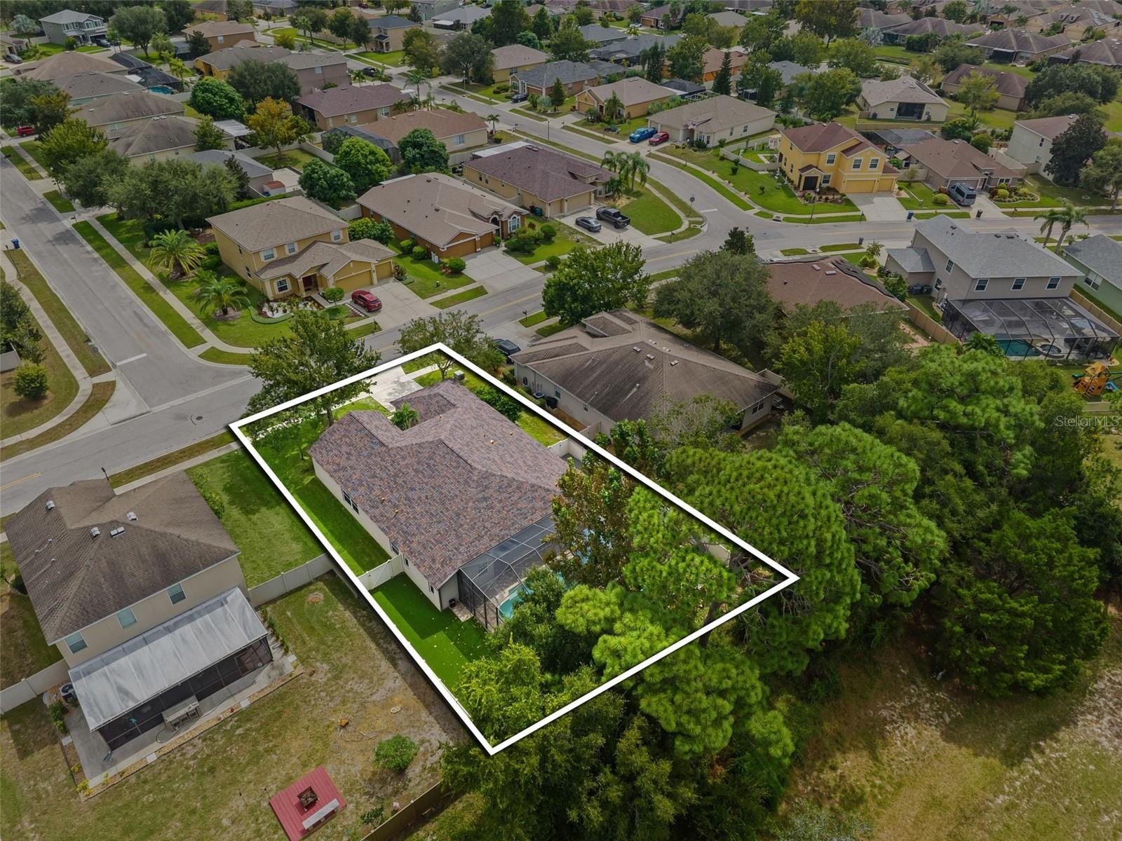 The aerial perspective really tells the story: a generous homesite, screened pool, fenced yard, and wooded privacy with no rear neighbors.