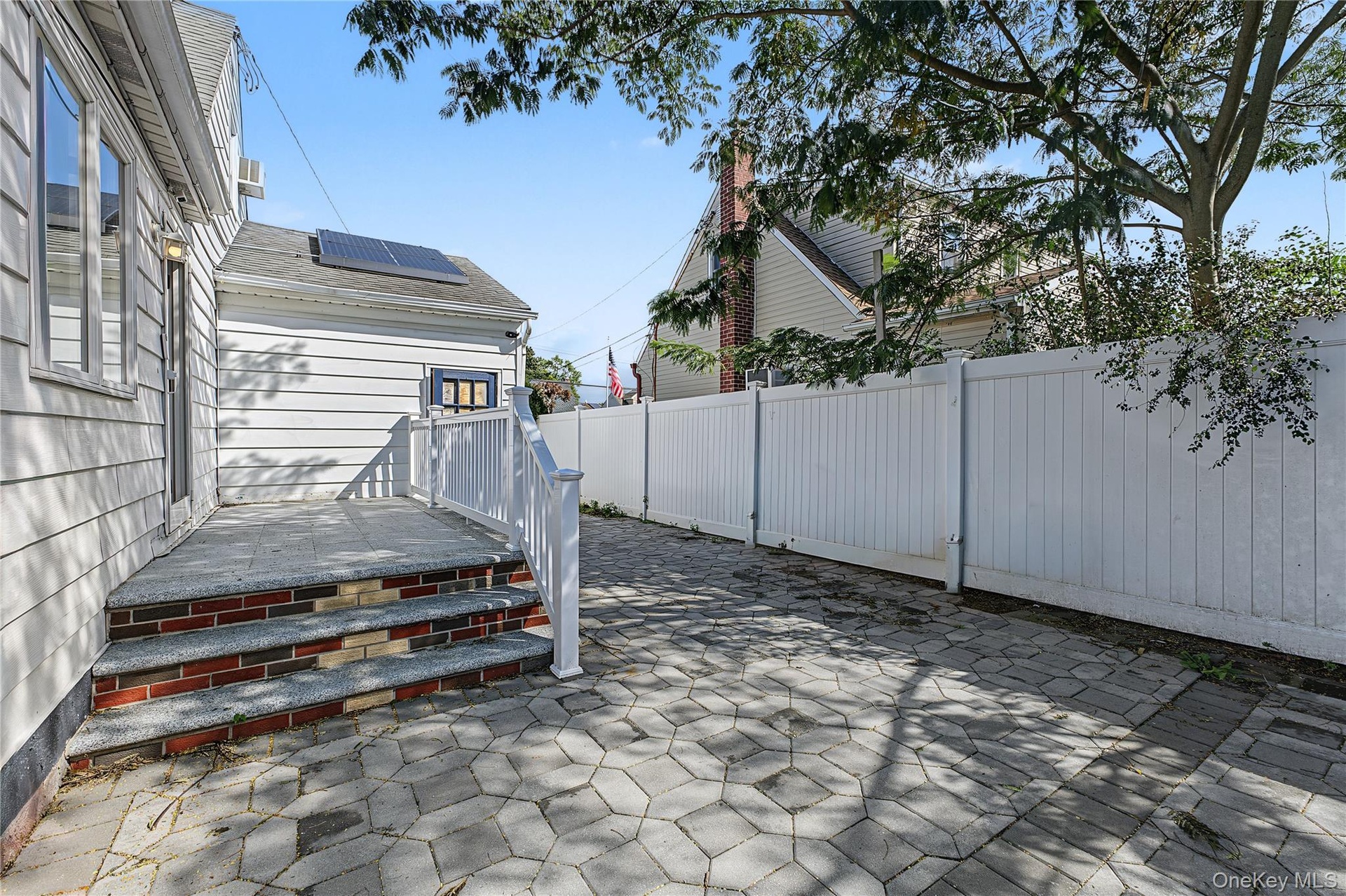 Paver patio area with a white privacy fence and exterior steps featuring brick and stone treads leading to the expansive kitchen/Dining Room