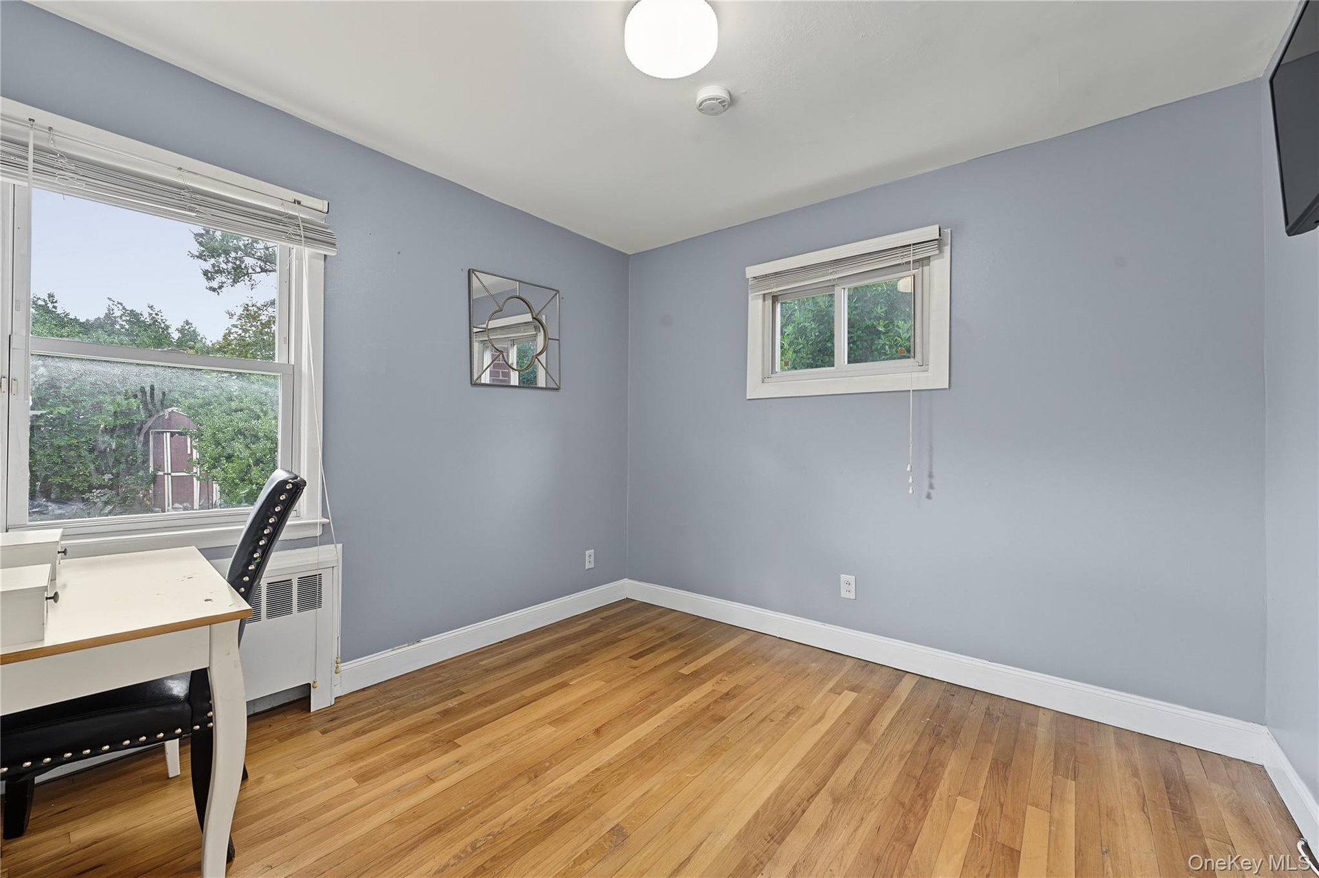 Second bedroom located on first floor with Hardwood flooring , two windows for natural light, and a white ceiling with a flush-mount light fixture