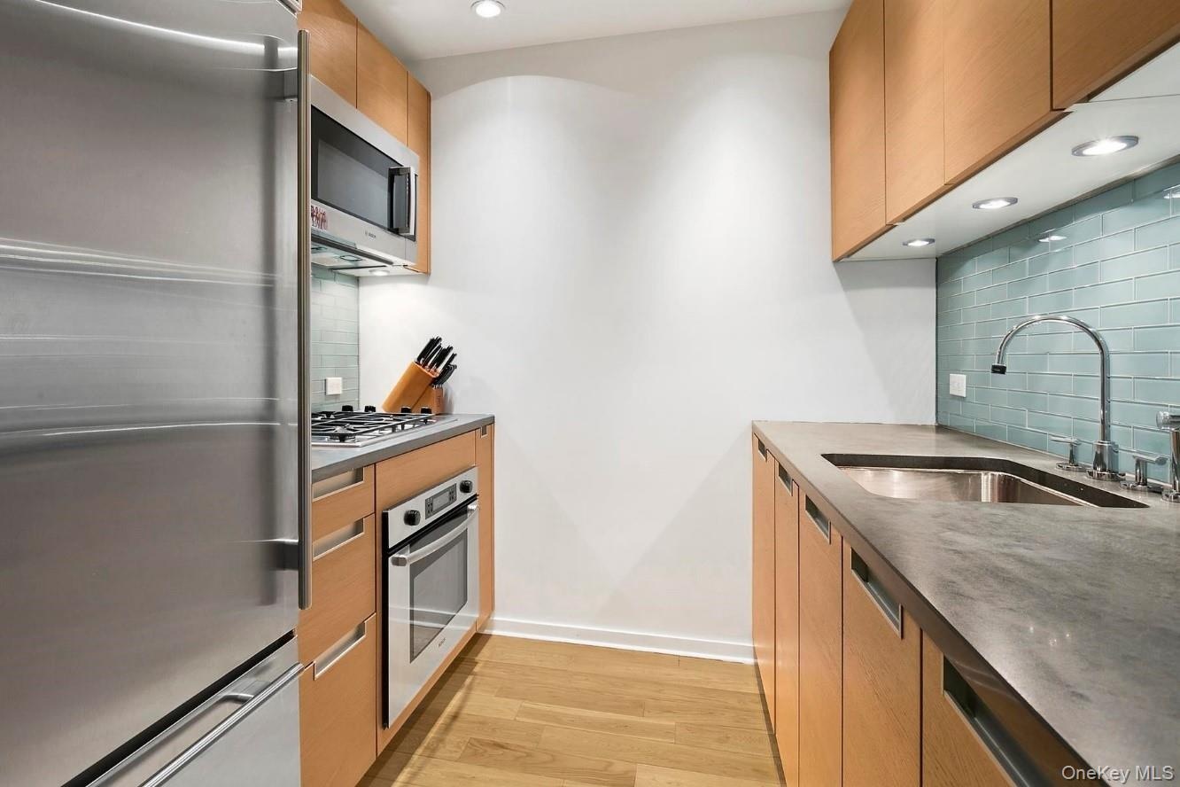 Kitchen with decorative backsplash, baseboards, appliances with stainless steel finishes, a sink, and light wood-style floors