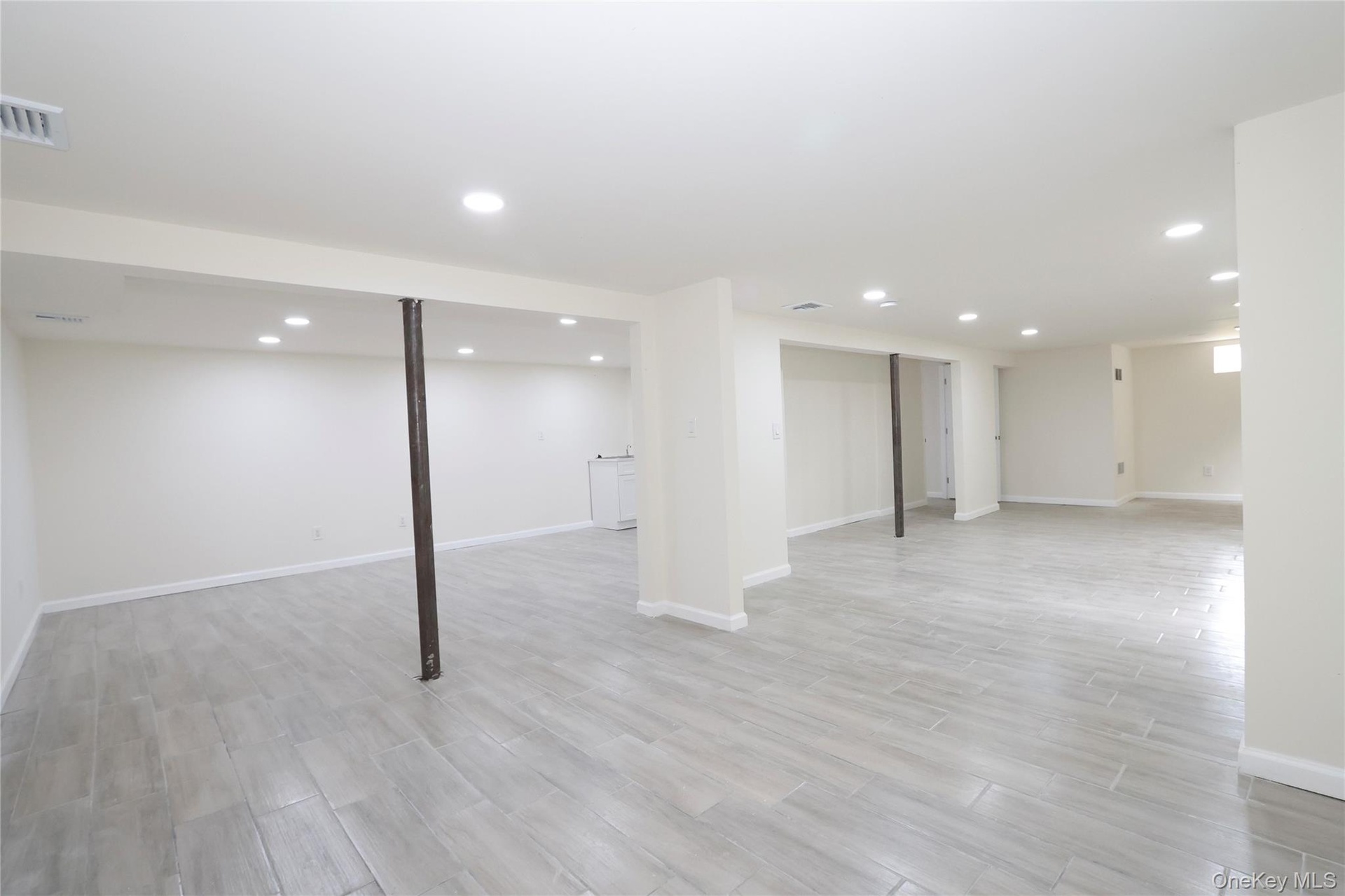 Spacious finished lower level with recessed lighting, tiled flooring, and a built-in sink cabinet