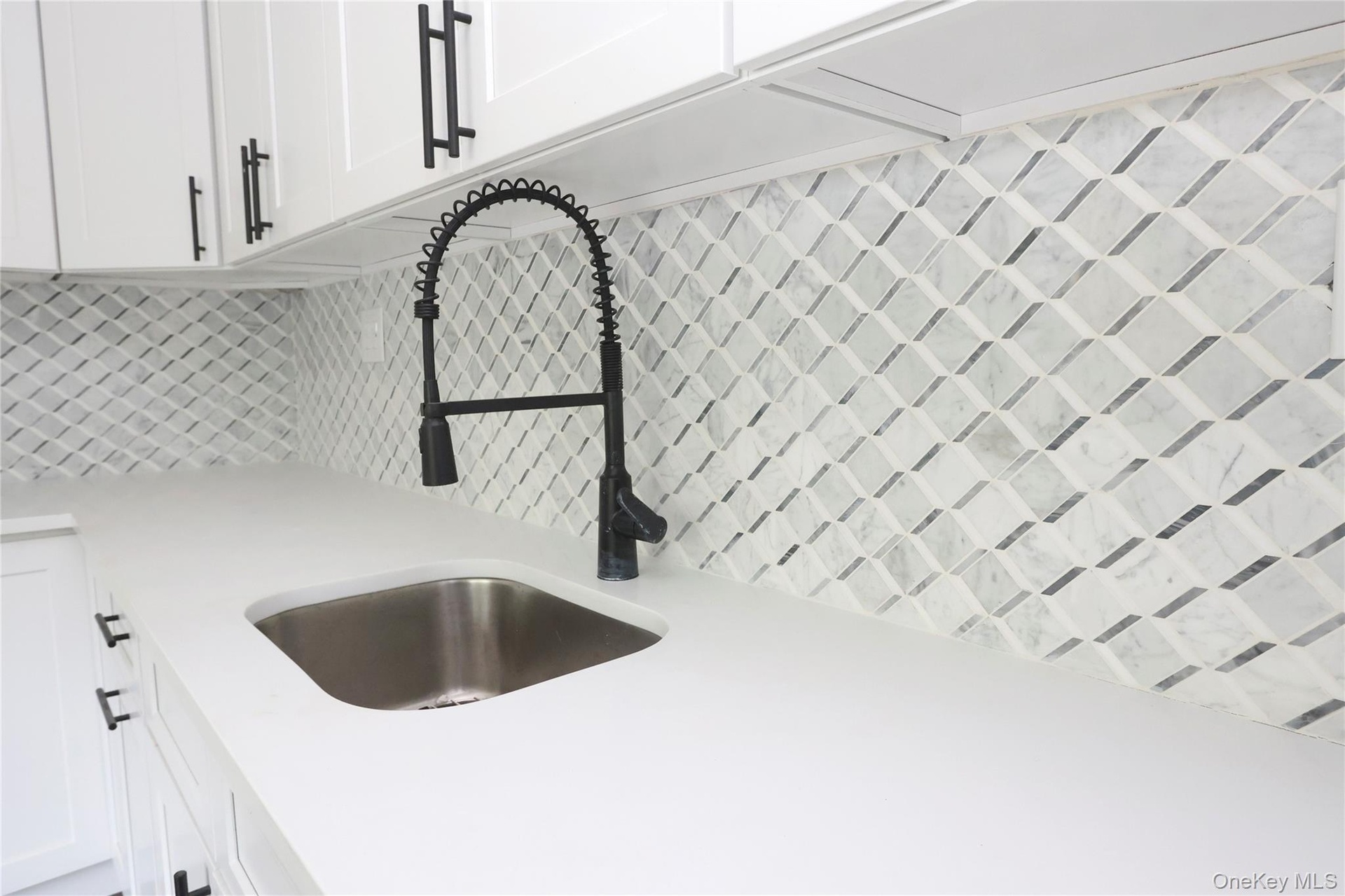 White cabinetry with matte black pulls, solid surface countertop, stainless steel undermount sink, matte black pull-down faucet, and geometric pattern