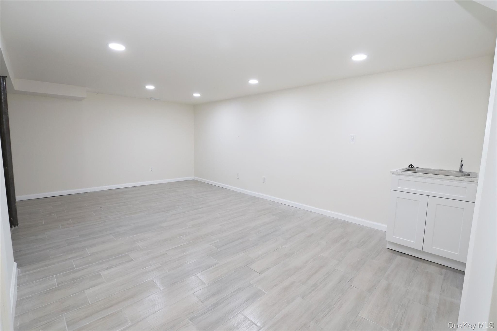 Open concept room featuring recessed lighting, light-toned plank flooring, and a built-in cabinet with a countertop and sink