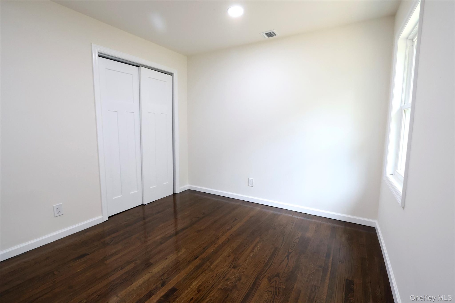 Hardwood flooring, recessed lighting, white trim, white walls, and a window providing natural illumination