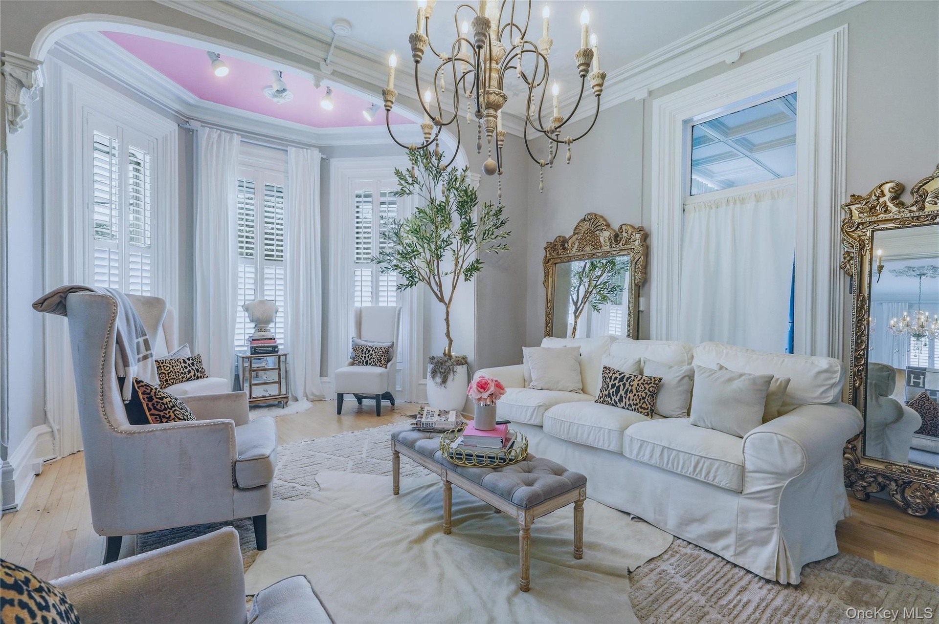Hardwood flooring, bay window with plantation shutters, coffered ceiling, ornate chandelier, and decorative wall mirrors