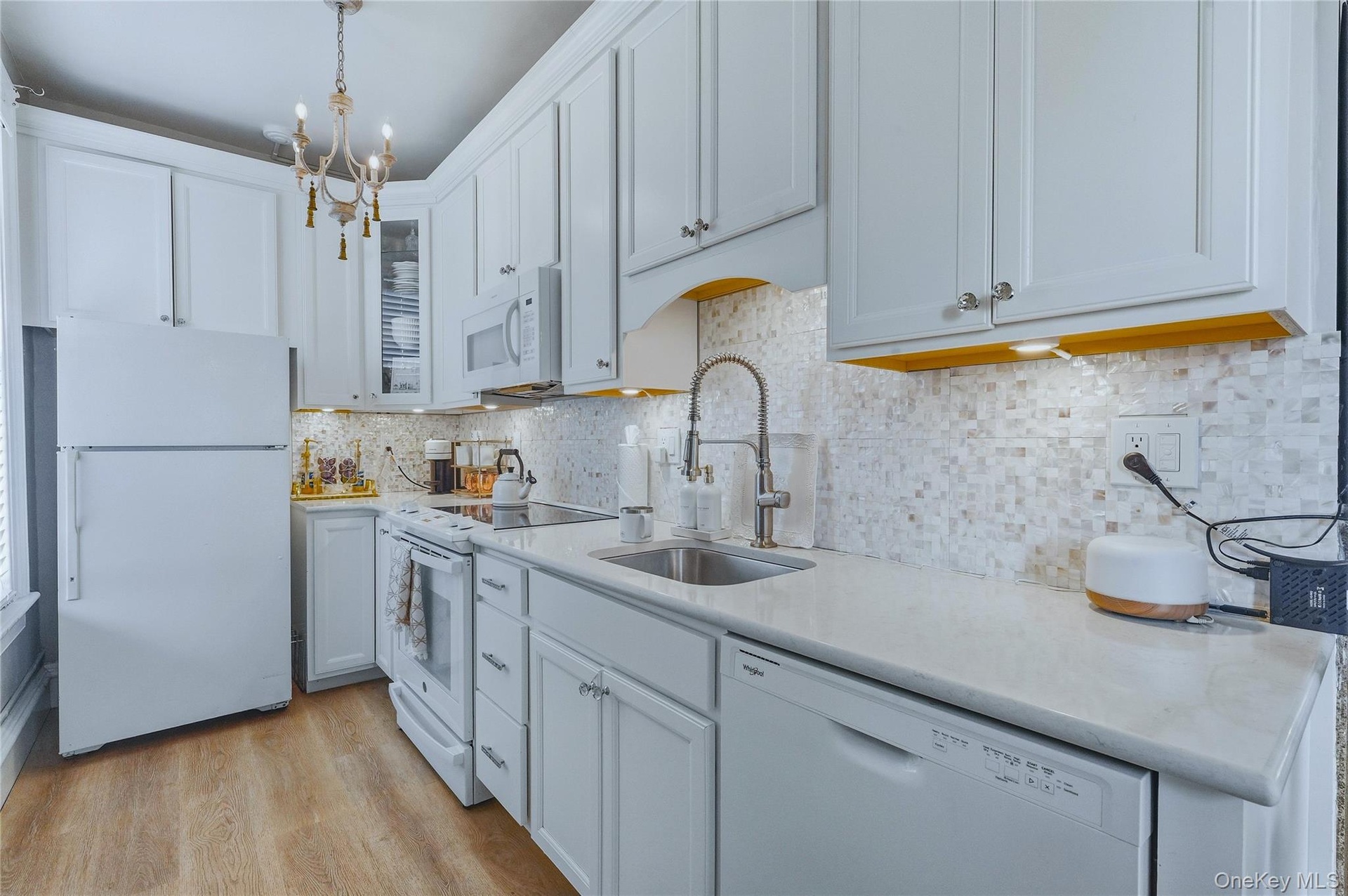 White kitchen cabinetry, stainless steel sink with a high-arc faucet, mosaic tile backsplash, light-colored countertops, and wood-finish flooring