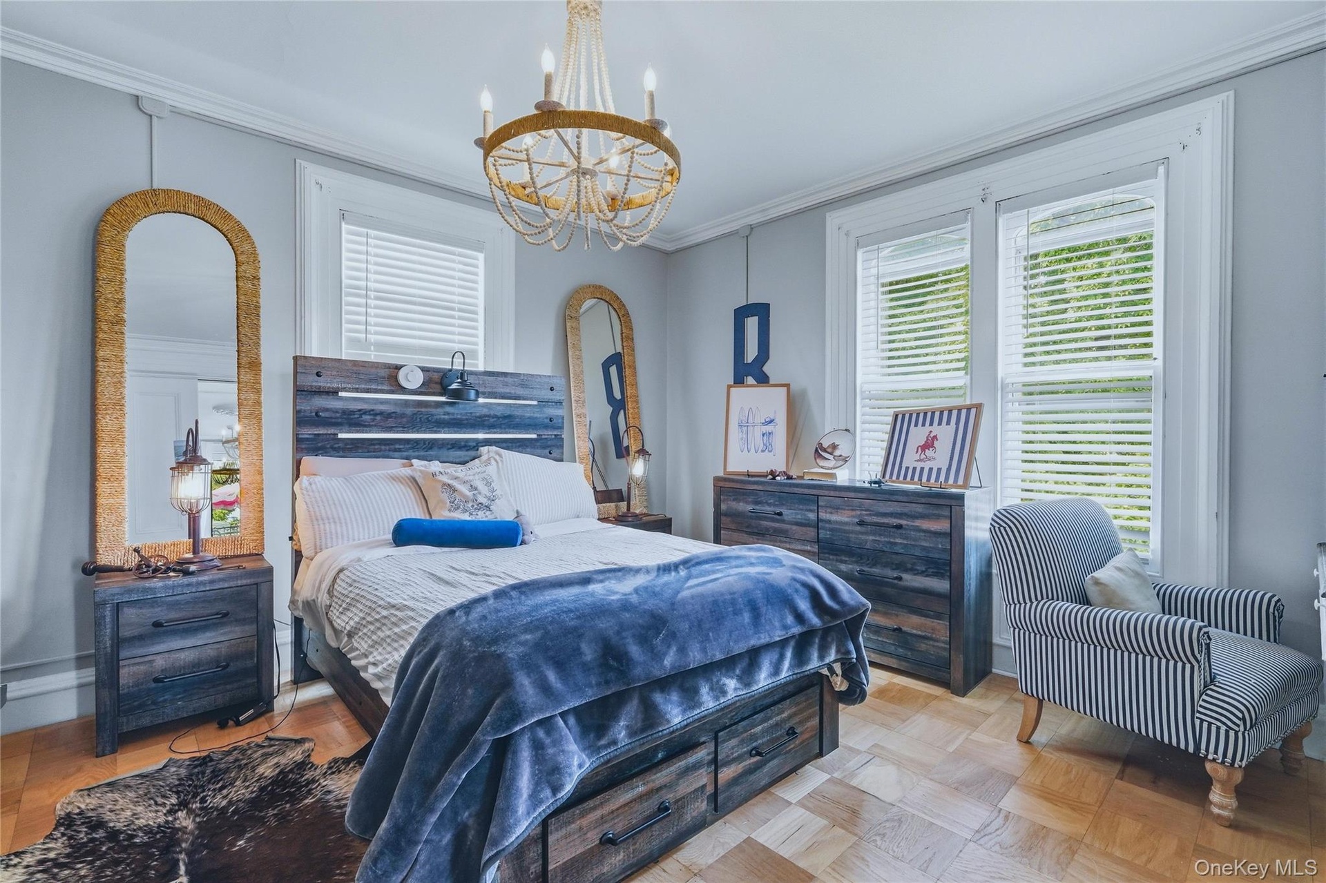 Light-colored wood-finish flooring, two large windows with blinds, crown molding, and a decorative chandelier