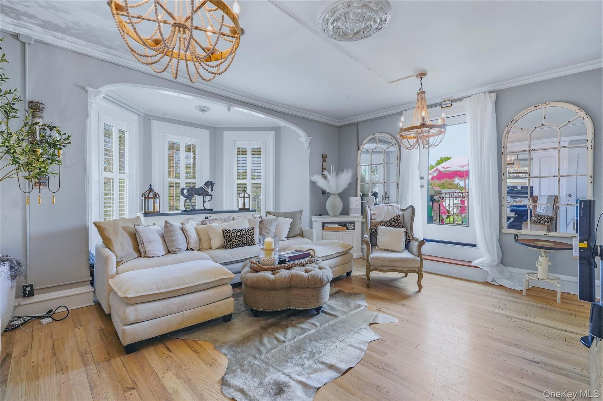 Wood-finish flooring throughout, bay window with plantation shutters, decorative ceiling medallions, and a decorative beaded chandelier