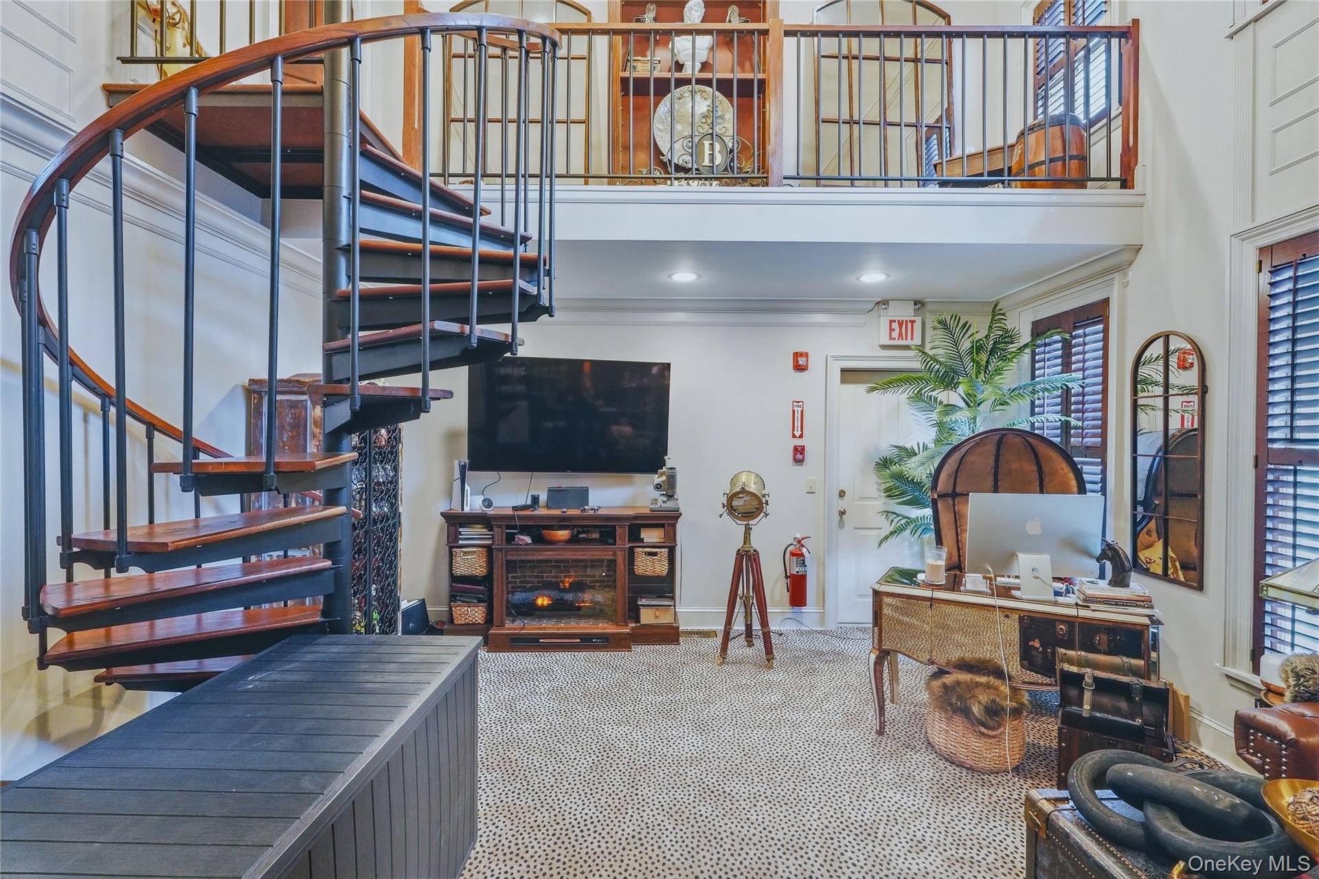 Spiral staircase with wood treads and metal balusters, upper-level balcony with metal railing, built-in media console, interior shutters on windows, a