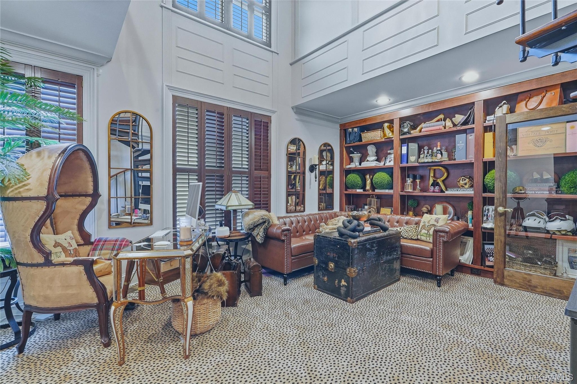 Two-story room featuring extensive built-in wooden shelving, dark wood plantation shutters, and a spiral staircase