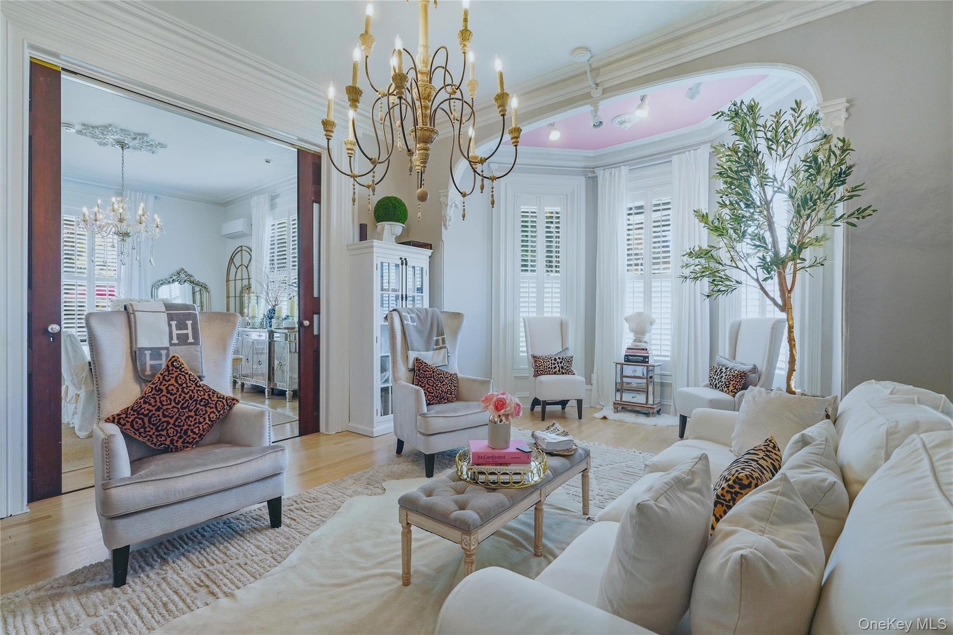 Hardwood flooring, ornate crown molding, decorative chandelier, bay window with plantation shutters, and an arched entry