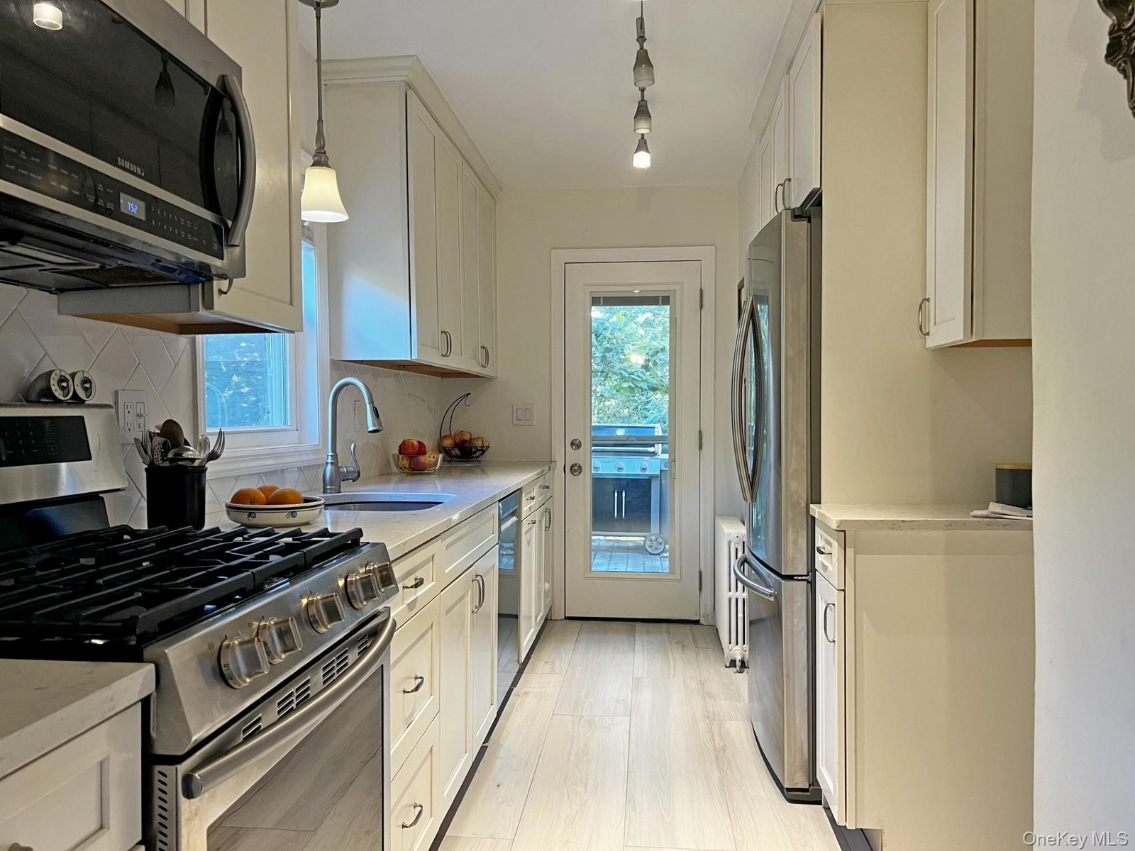 Kitchen with appliances with stainless steel finishes, pendant lighting, light stone counters, white cabinets, and light wood-style floors