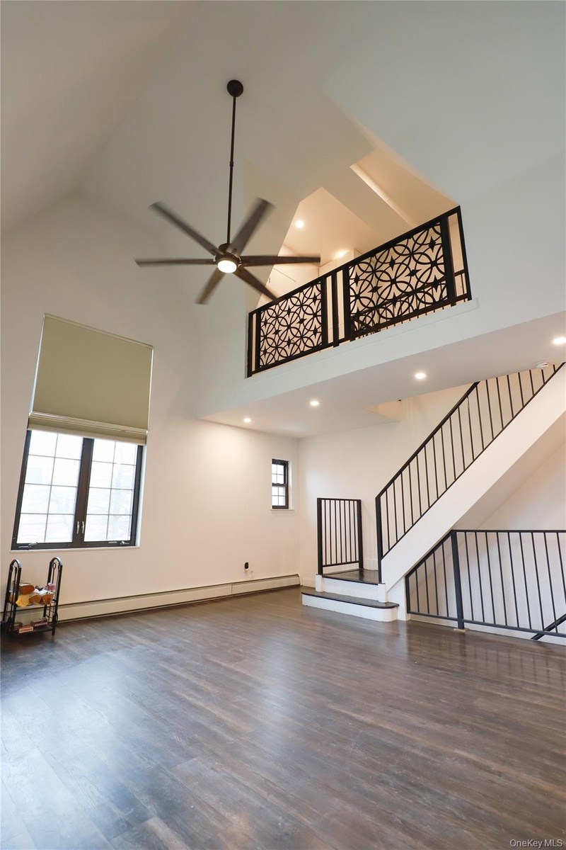 Soaring vaulted ceiling with a large ceiling fan, dark wood-finish flooring, and a decorative wrought iron balcony