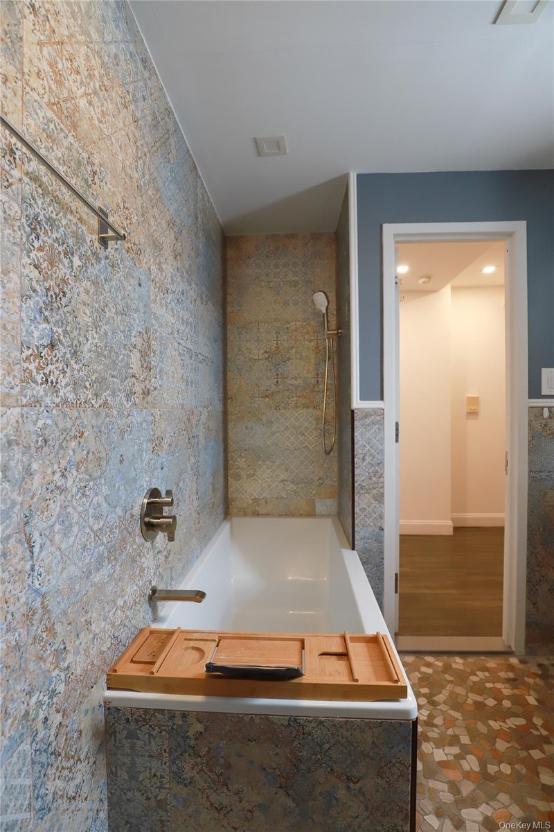 Built-in bathtub with brushed nickel fixtures, patterned tile surround, and a handheld showerhead