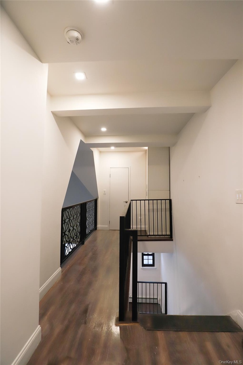 Hall with dark wood-style flooring and recessed lighting. Overlooks the living room space with vaulted ceilings.