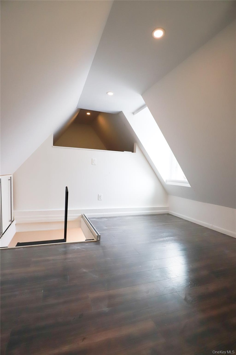 Sloped ceilings with recessed lighting, dark wood-finish flooring, and an integrated skylight