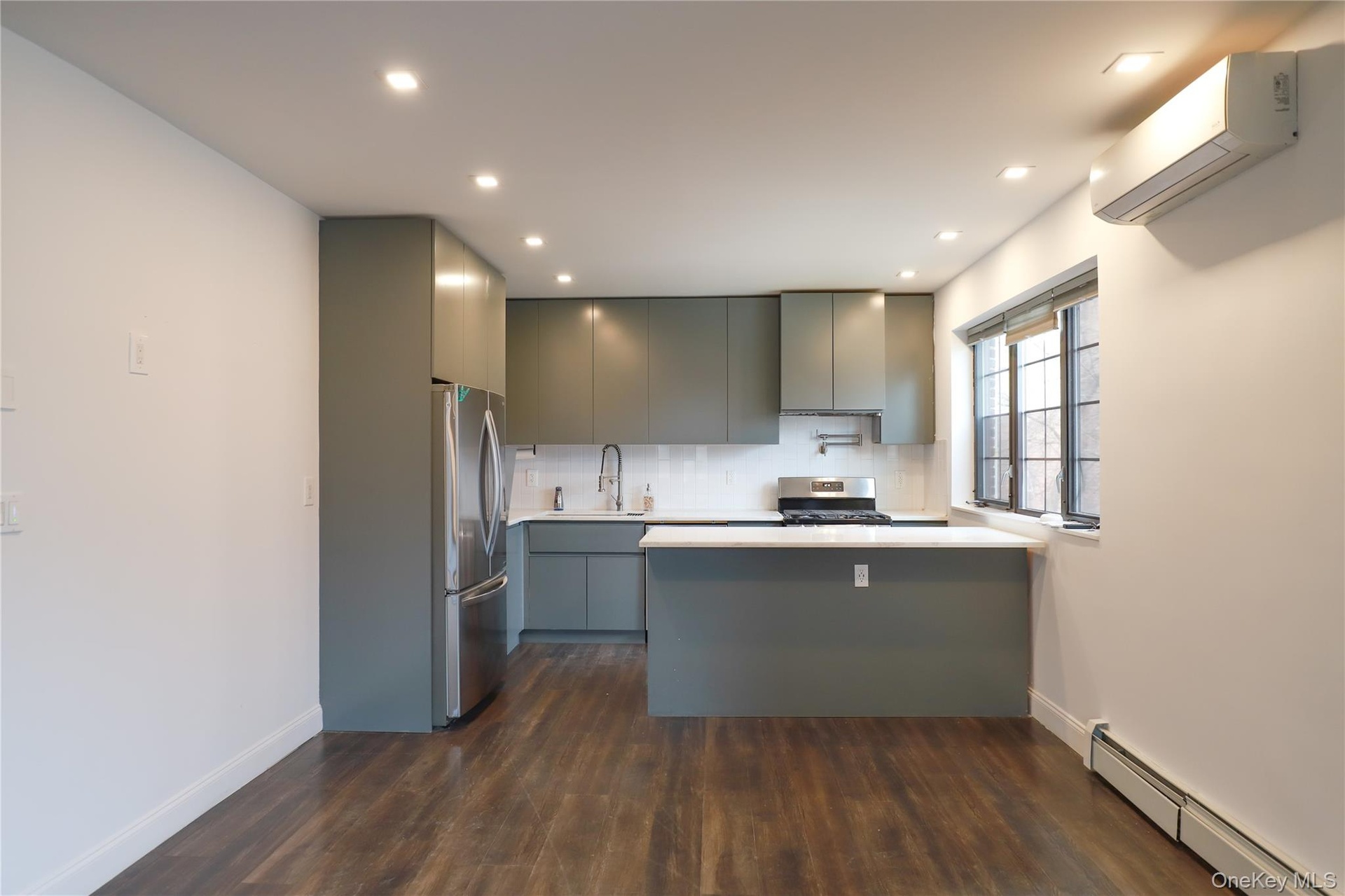 Kitchen featuring sleek flat-panel cabinetry, stainless steel appliances, white subway tile backsplash, and wood-finish flooring
