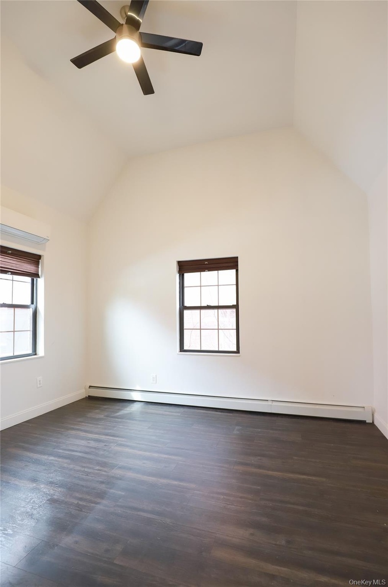 Vaulted ceiling, wood-finish flooring, two windows, two-tone blinds, and a ceiling fan with integrated lighting