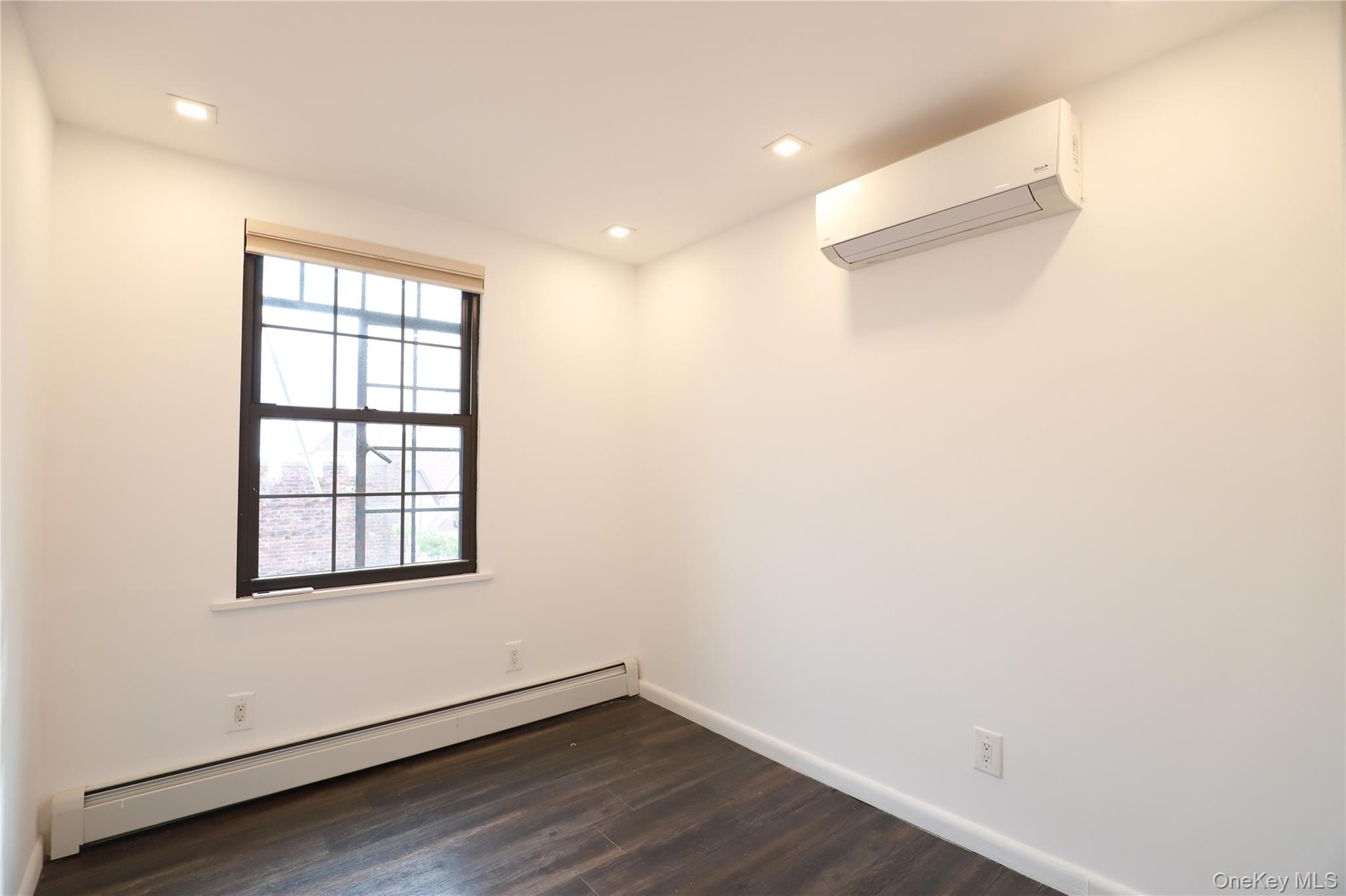 Recessed ceiling lighting, dark wood-finish flooring, and a wall-mounted mini-split HVAC unit
