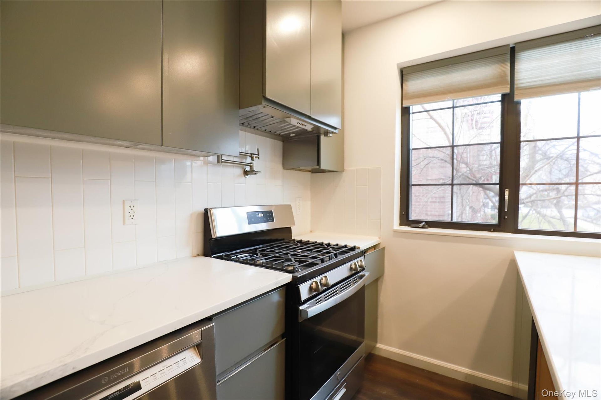 Kitchen featuring appliances with stainless steel finishes, sage green cabinetry, light stone counters, pot filler, and under cabinet hood range