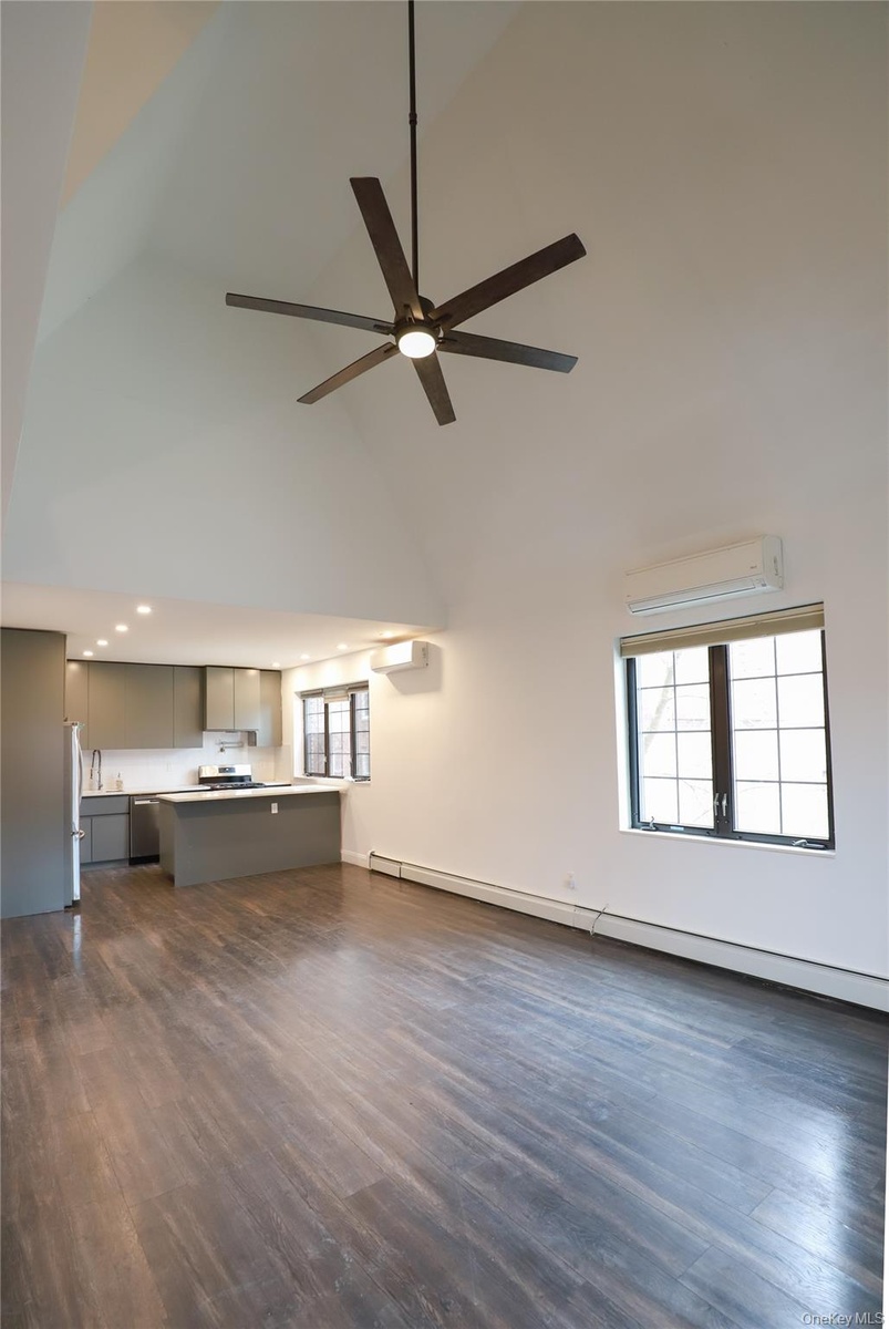 Vaulted ceiling with a large ceiling fan, dark wood-finish flooring, a kitchen island with seating, recessed lighting, and a ductless mini-split syste