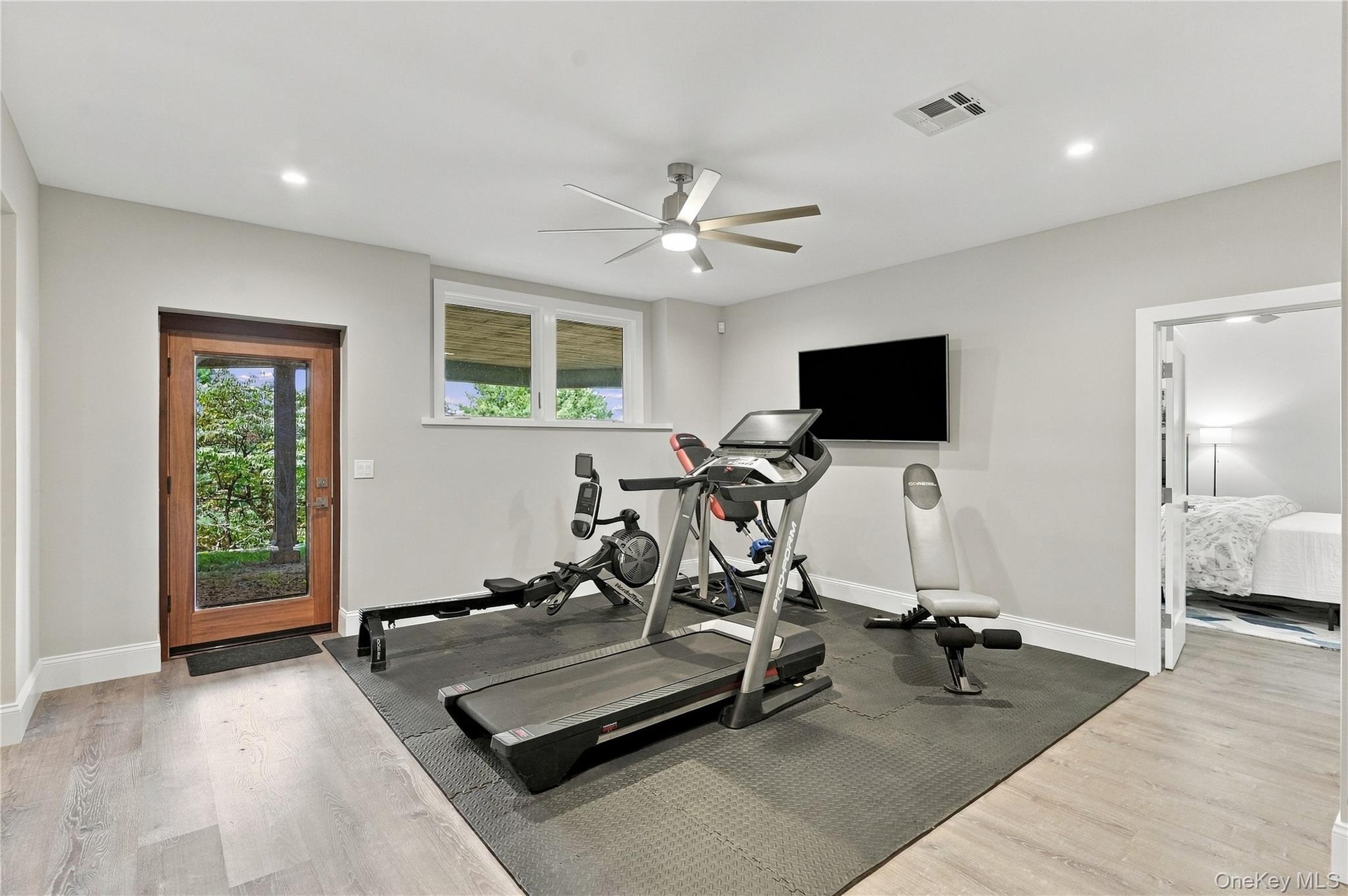 A spacious lower-level home gym featuring dedicated workout space, natural light, and direct access to the outdoors, offering the convenience of fitne