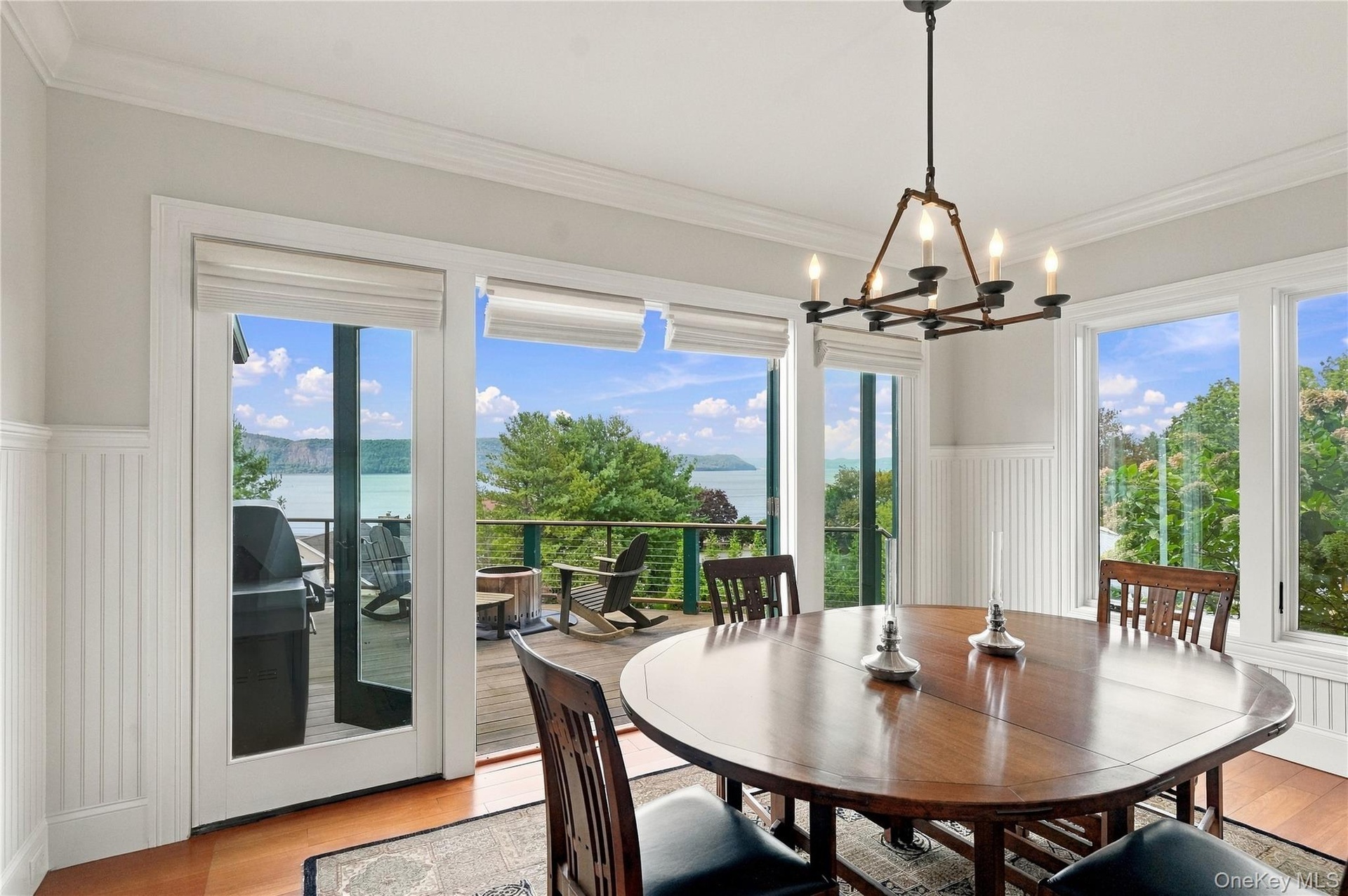 An oversized breakfast room surrounded by walls of glass, offering breathtaking Hudson River views and direct access to the expansive outdoor deck. Th