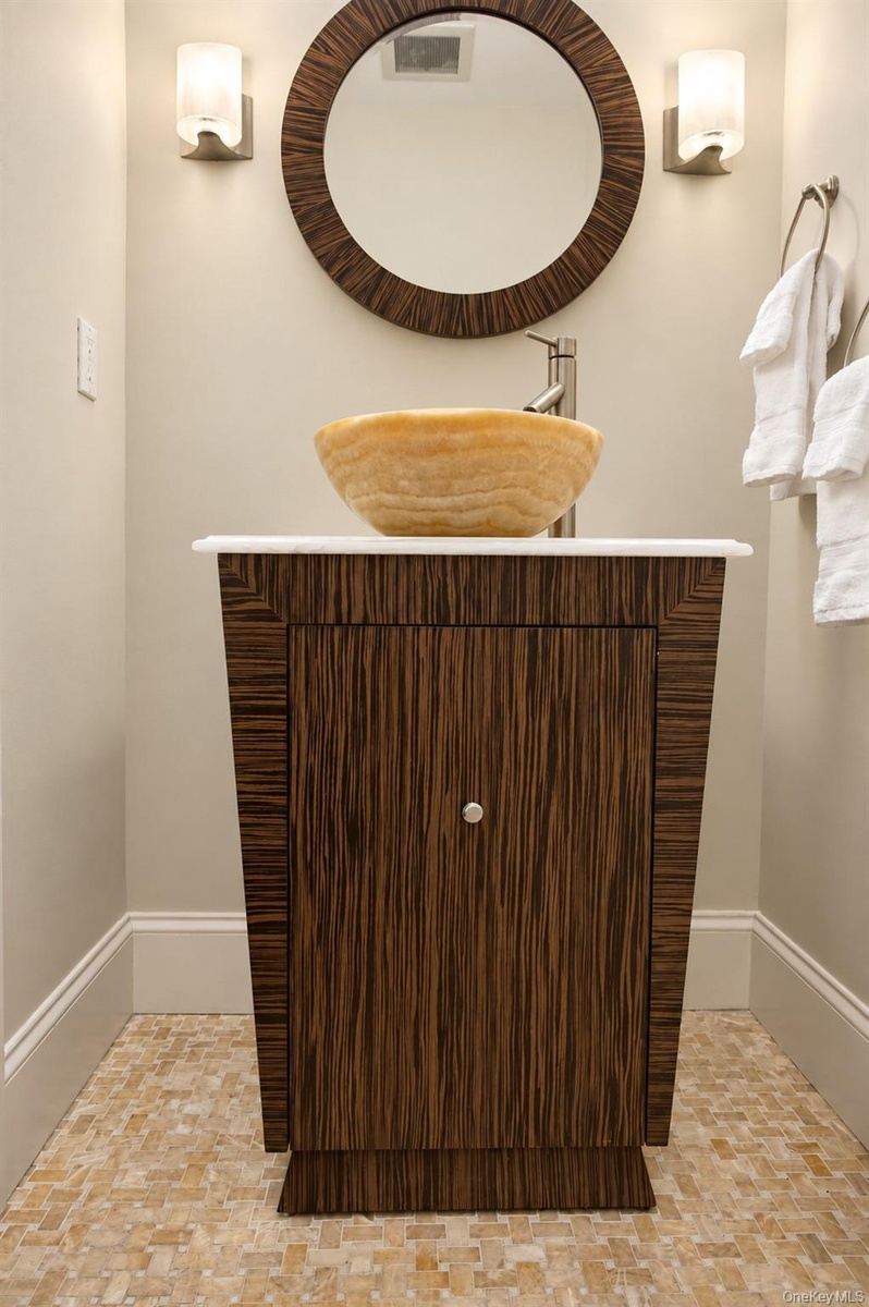 An exquisitely designed powder room featuring a striking honey and white onyx vessel sink, custom wood vanity, and elegant finishes that reflect the h