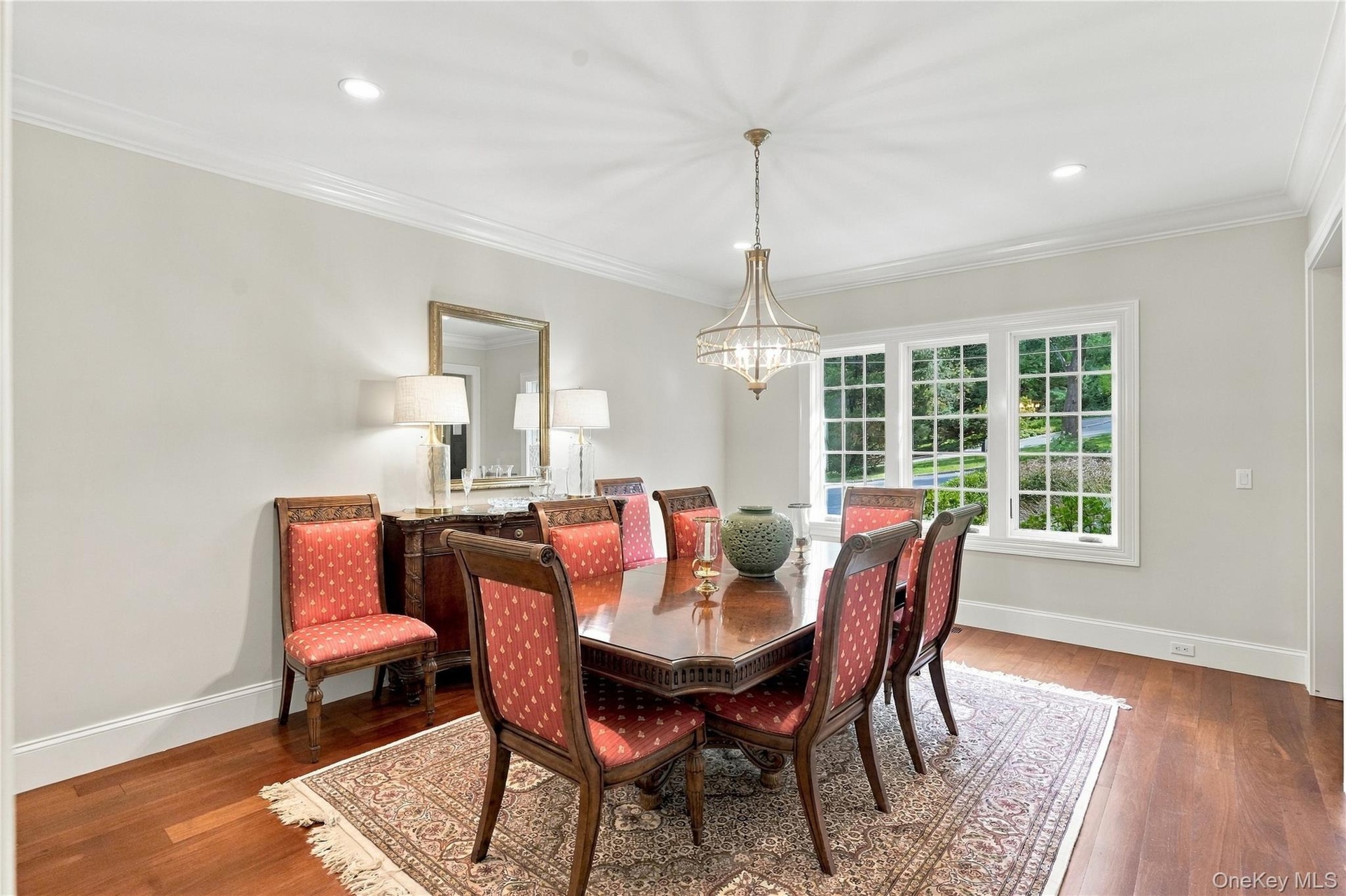 An elegant formal dining room featuring crown molding, rich hardwood floors, a statement chandelier.