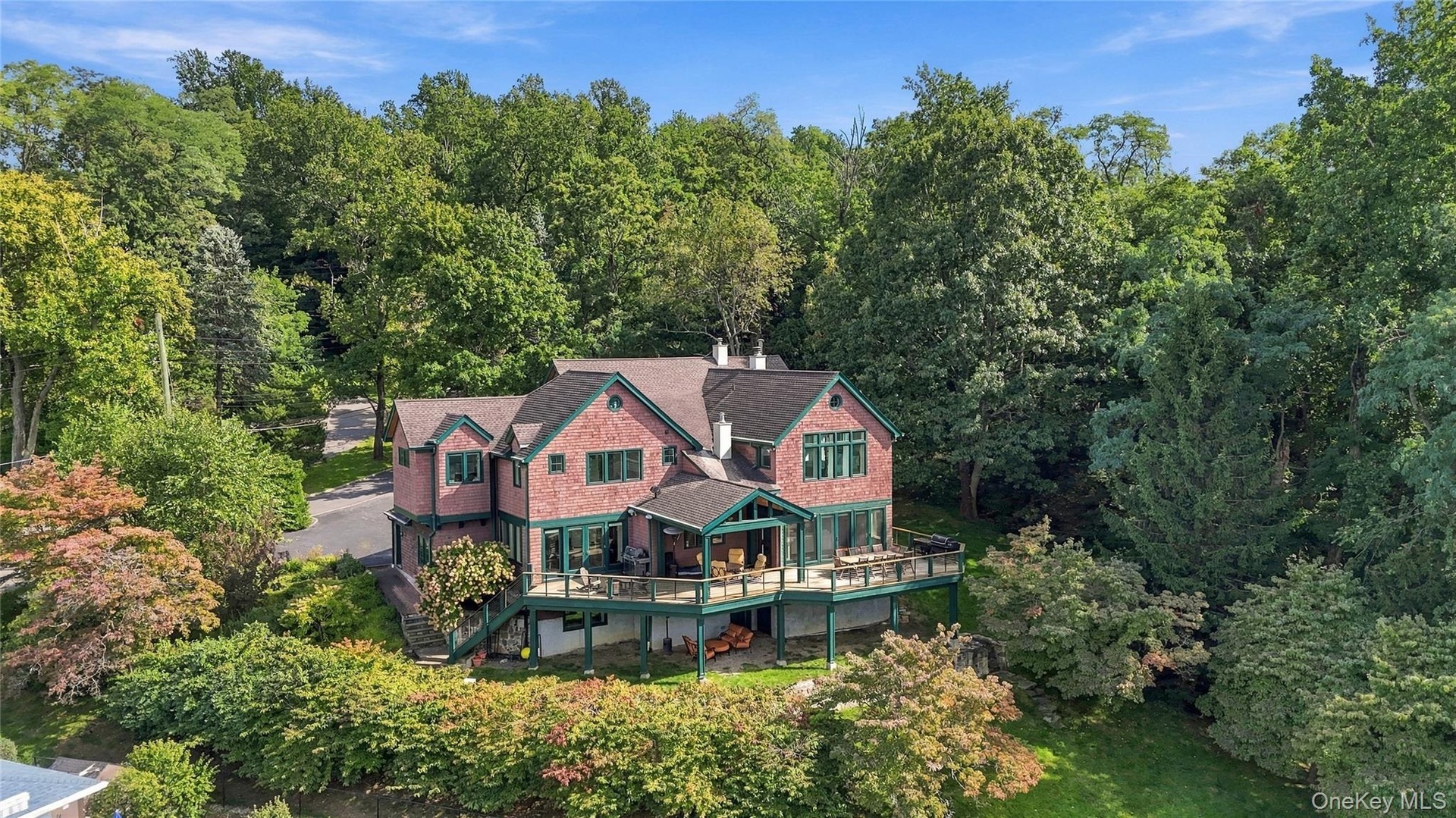 An impressive aerial view showcasing the home's striking architecture, expansive Ipe wood deck, covered outdoor lounge, and lush surrounding landscape