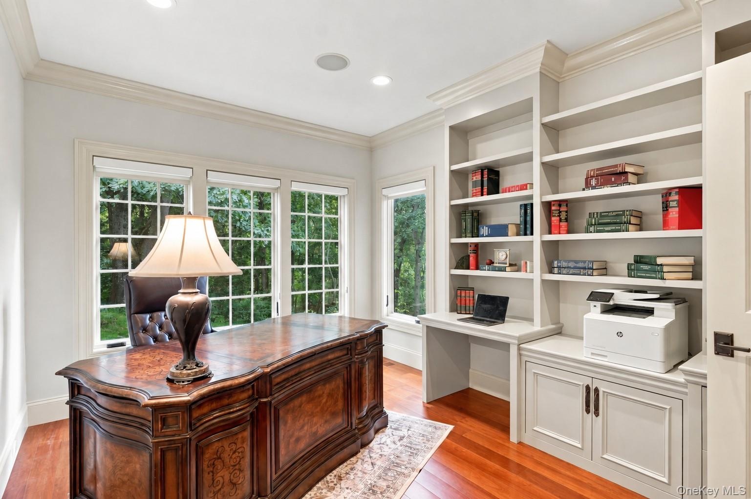 A beautifully appointed private home office featuring custom built-in shelving, integrated file cabinets, dedicated workspace, and expansive windows o