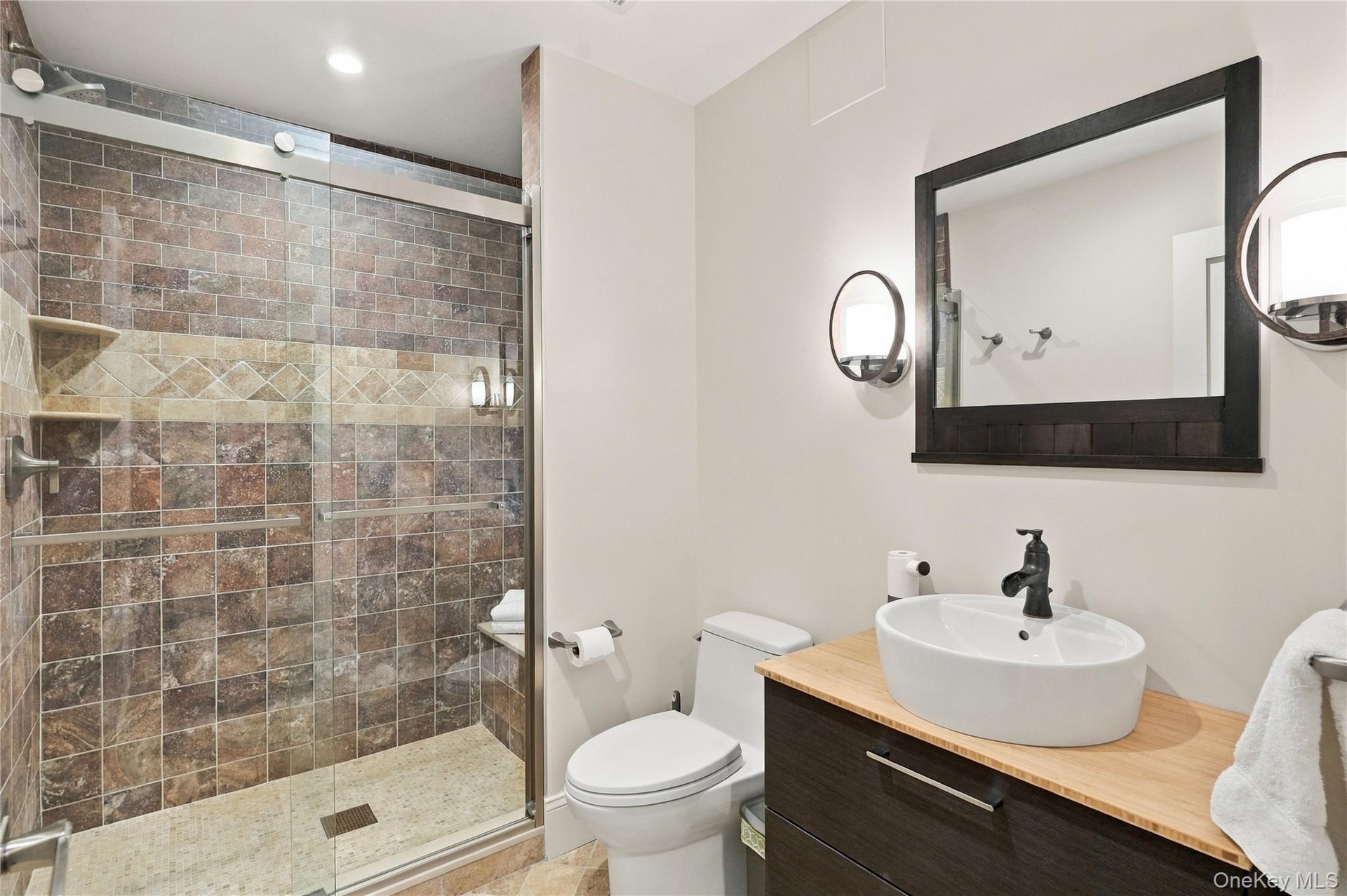A beautifully finished lower-level bathroom featuring a spacious glass-enclosed shower, custom vanity, and modern fixtures with tasteful custom finish