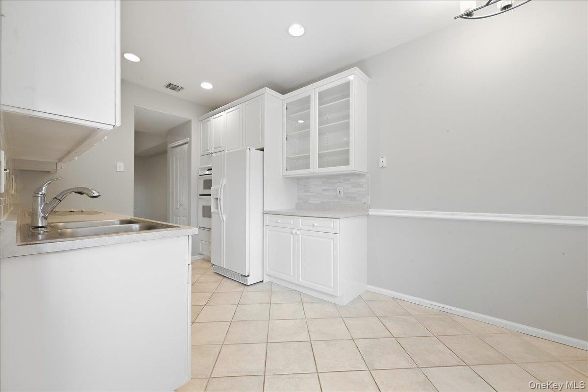 Kitchen featuring white cabinetry, stainless steel sink, tiled flooring, and built-in double ovens