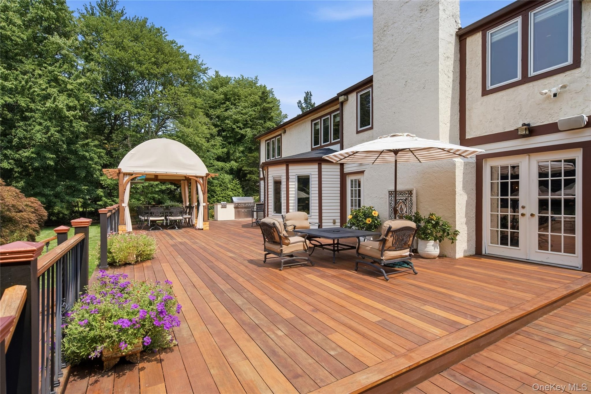 Expansive mahogany-finish deck with pergola  and built-in outdoor kitchen, and French doors providing direct access to the interior