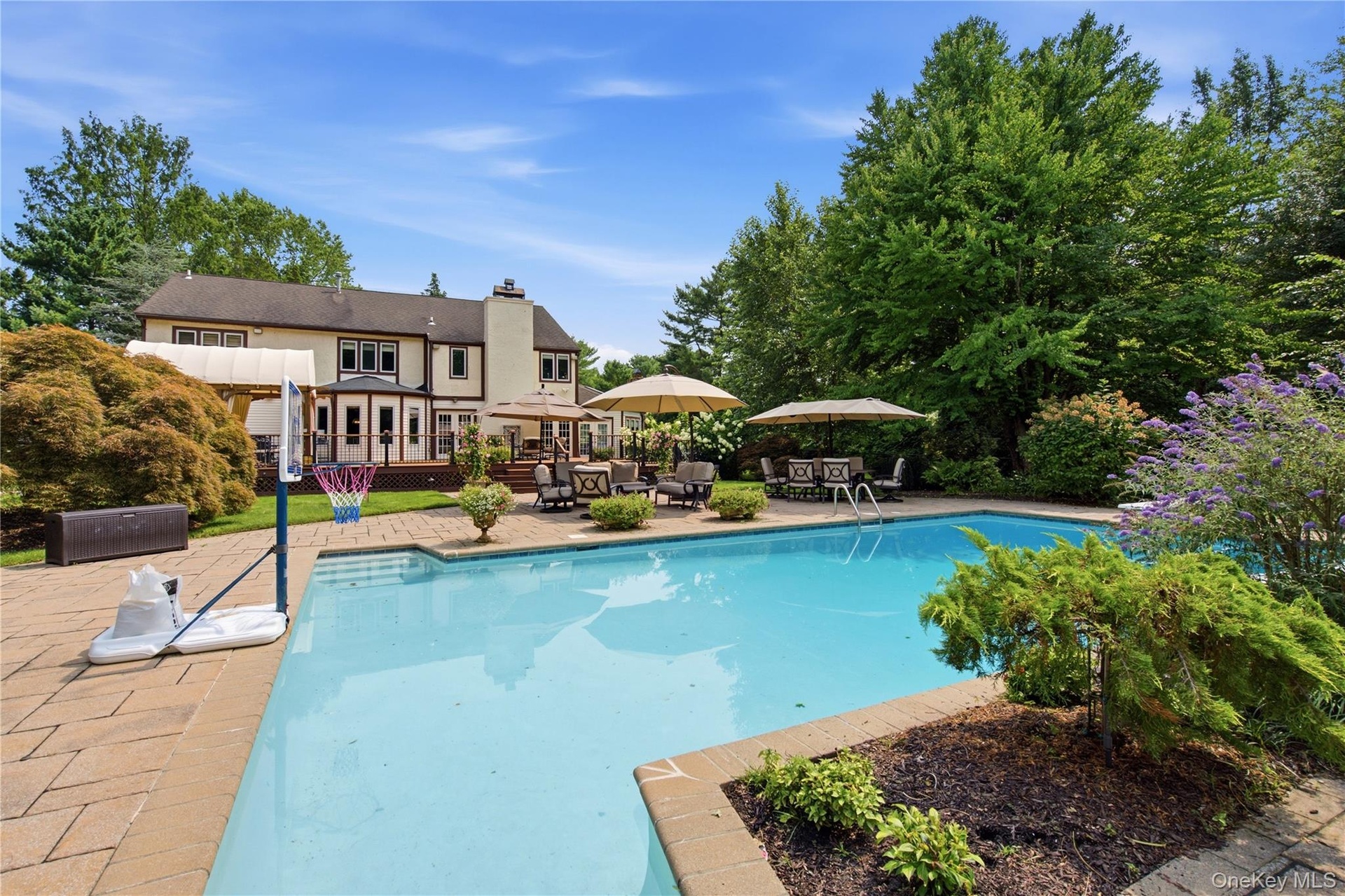 Expansive outdoor living area featuring a large swimming pool with a stone paver surround, a multi-level deck, mature landscaping, and a well-maintain