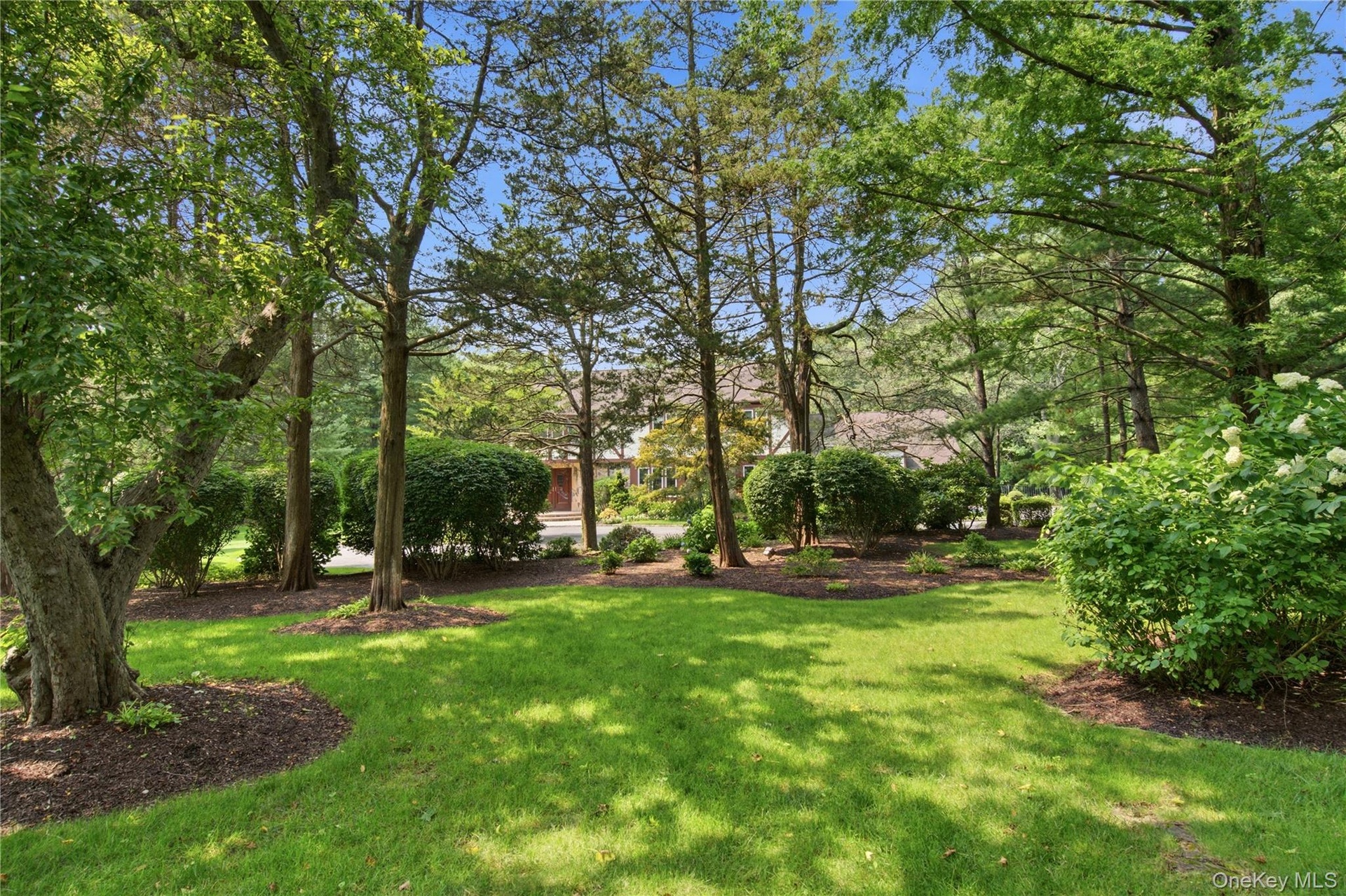 Manicured lawn with mature trees, established shrubbery, and mulched landscaping beds