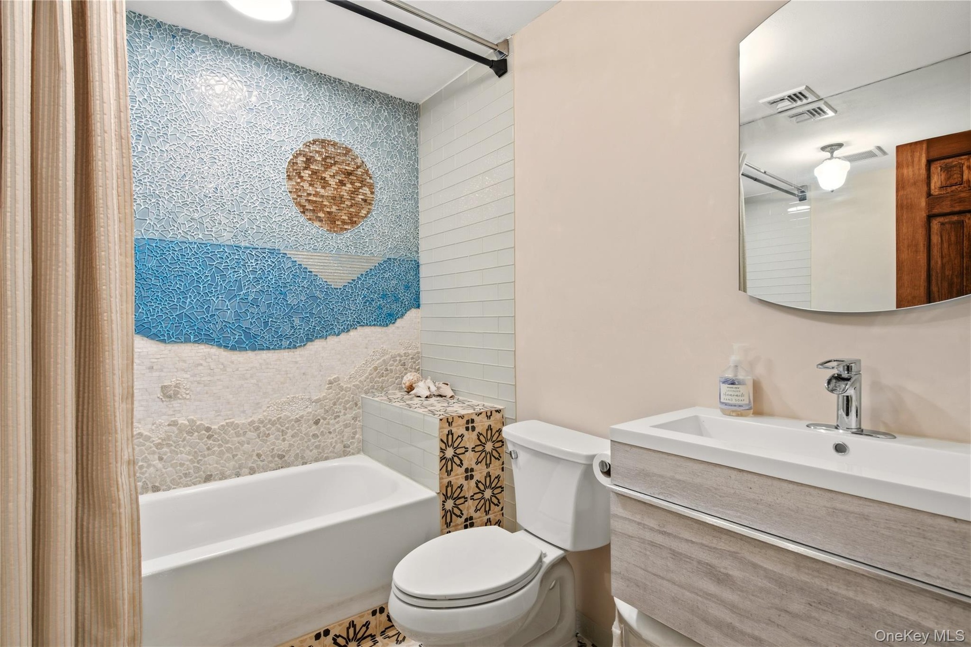 Bathtub with a mosaic-tiled accent wall, vanity with an integrated sink, and a wall-mounted mirror